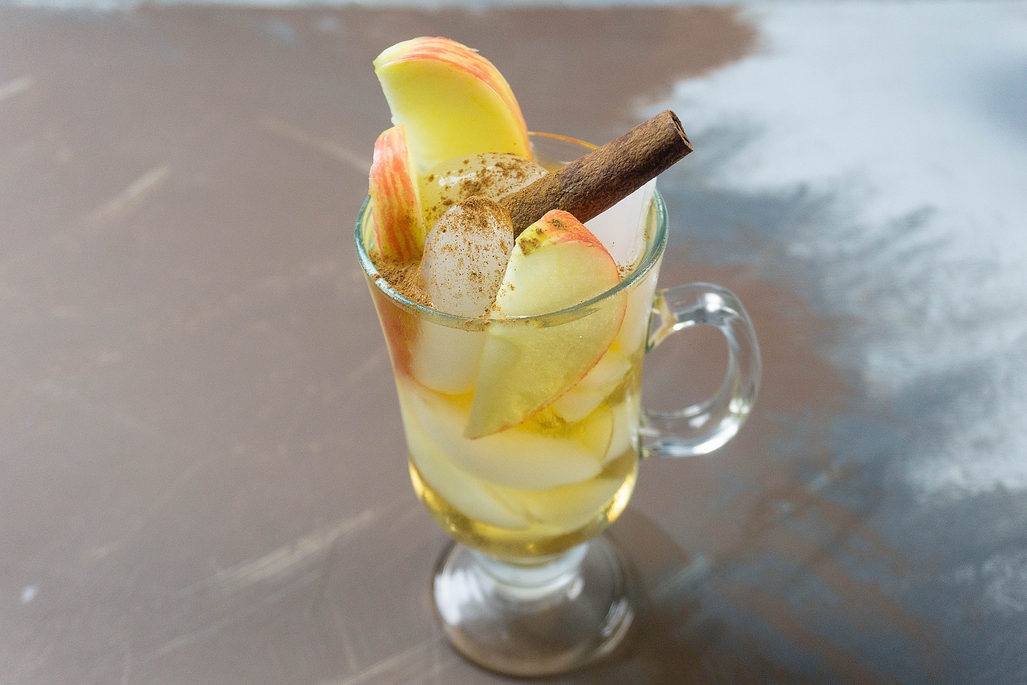 Caramel apple cocktail with apple slices and cinnamon in a glass.