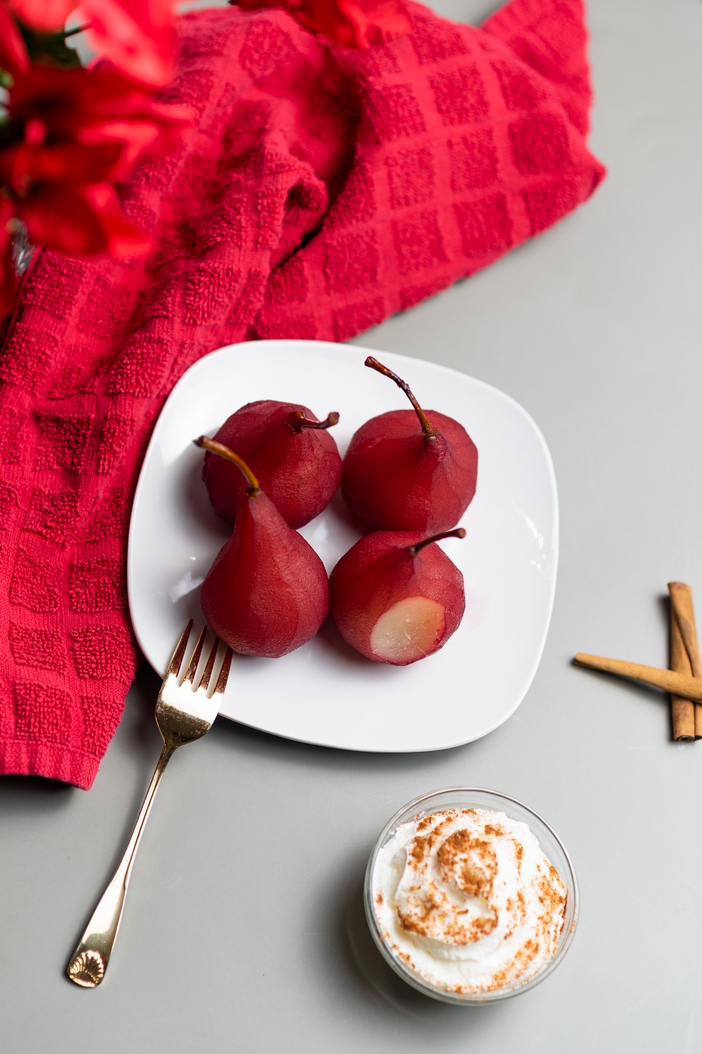 Red wine poached pears on a white plate with a gold fork.