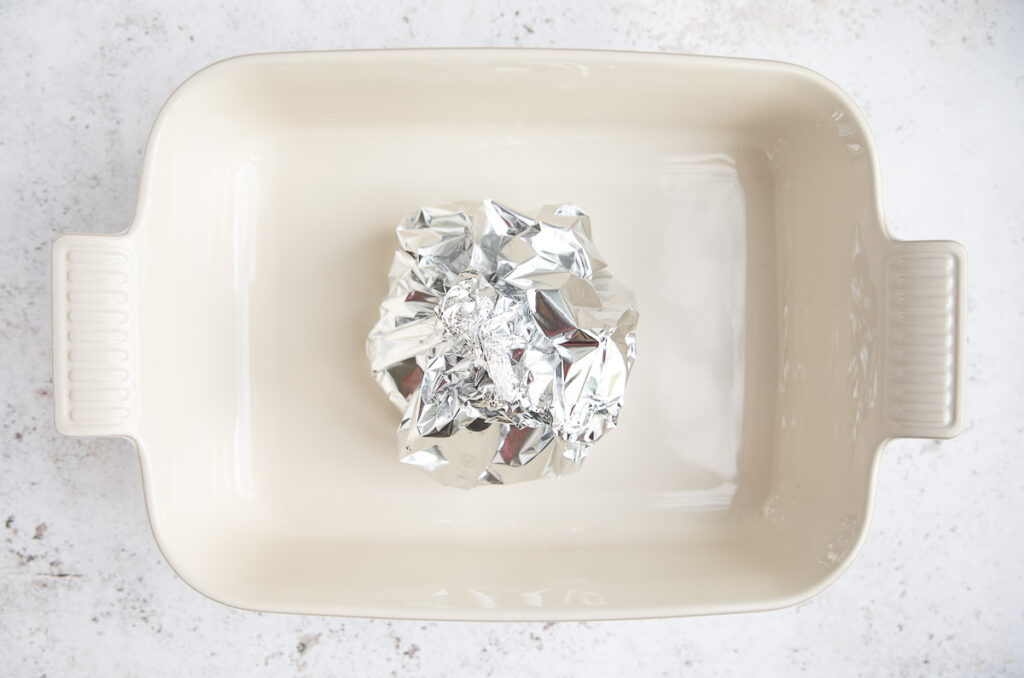 A wheel of cheese wrapped tightly in tin foil, then set in baking dish.