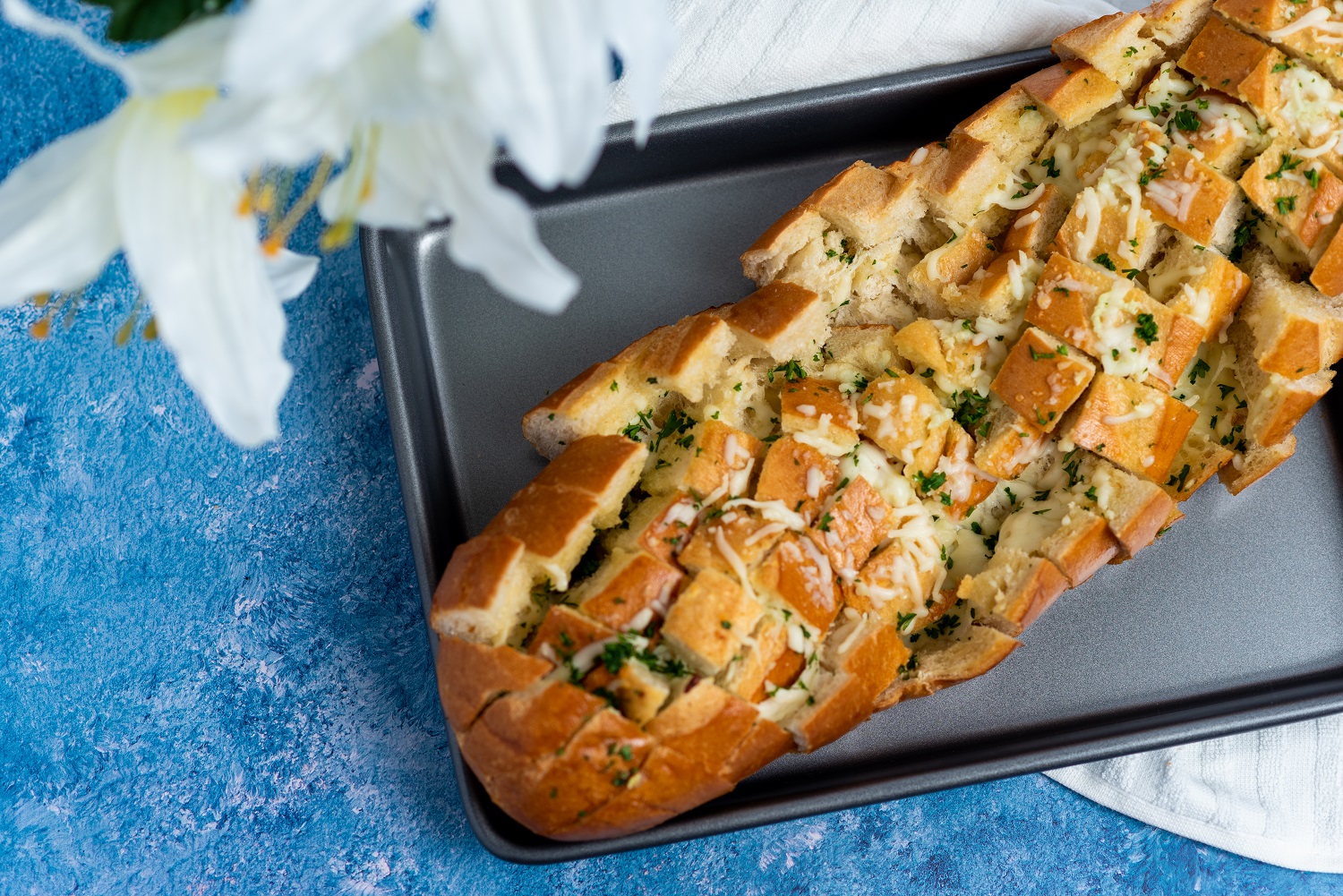 Garlic and Cheese pull apart bread on a baking sheet on a blue table.