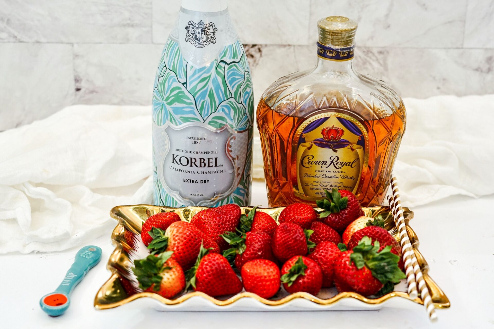 Champagne, whiskey, and strawberries on a white countertop.