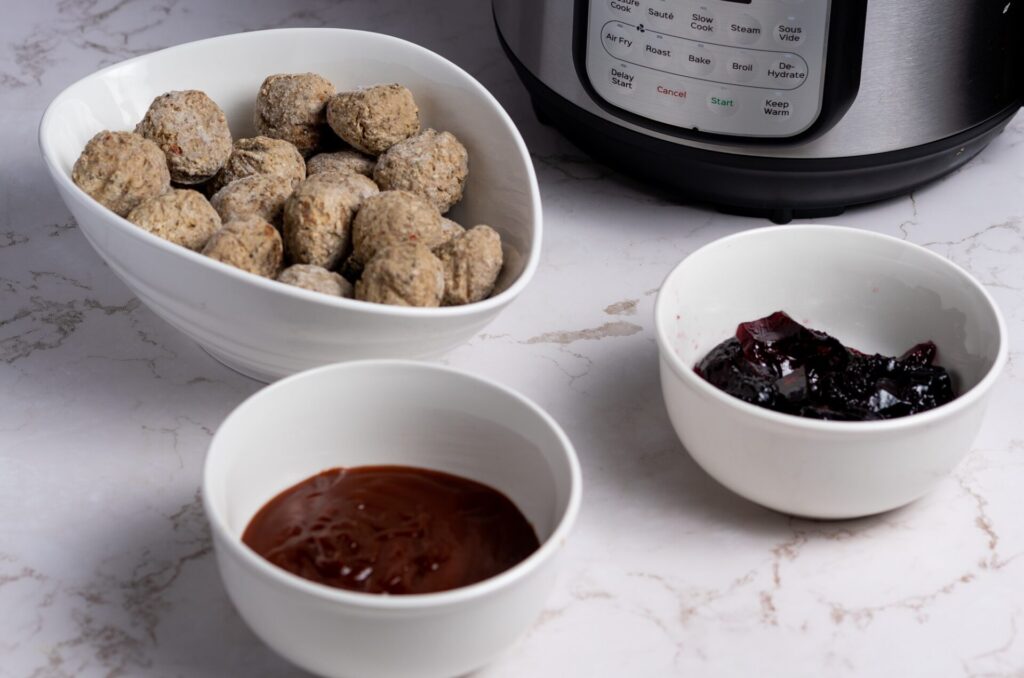 Frozen meatballs, grape jelly and barbeque sauce in bowls.