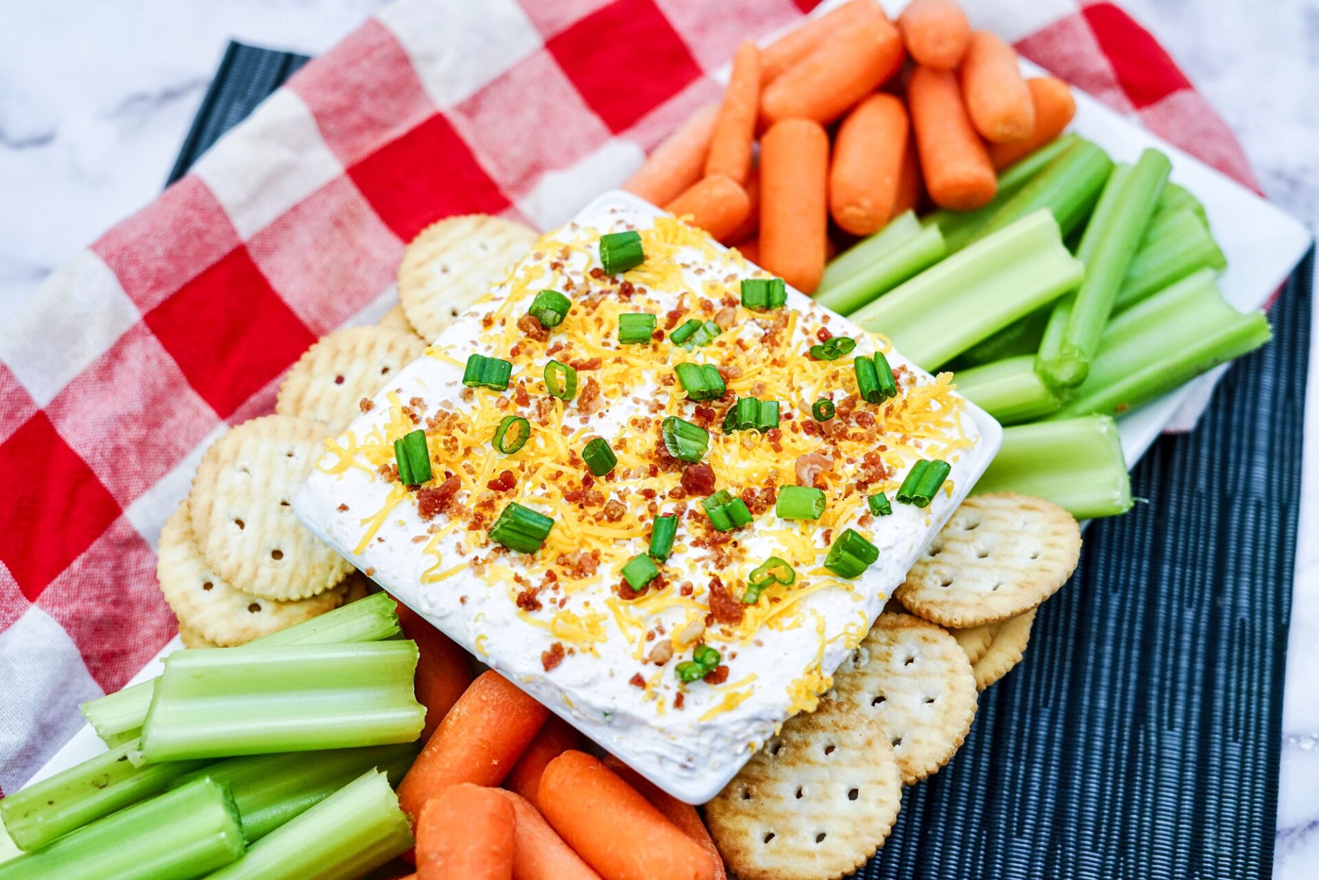 Bacon dip in a bowl surrounded with crackers and vegetables.