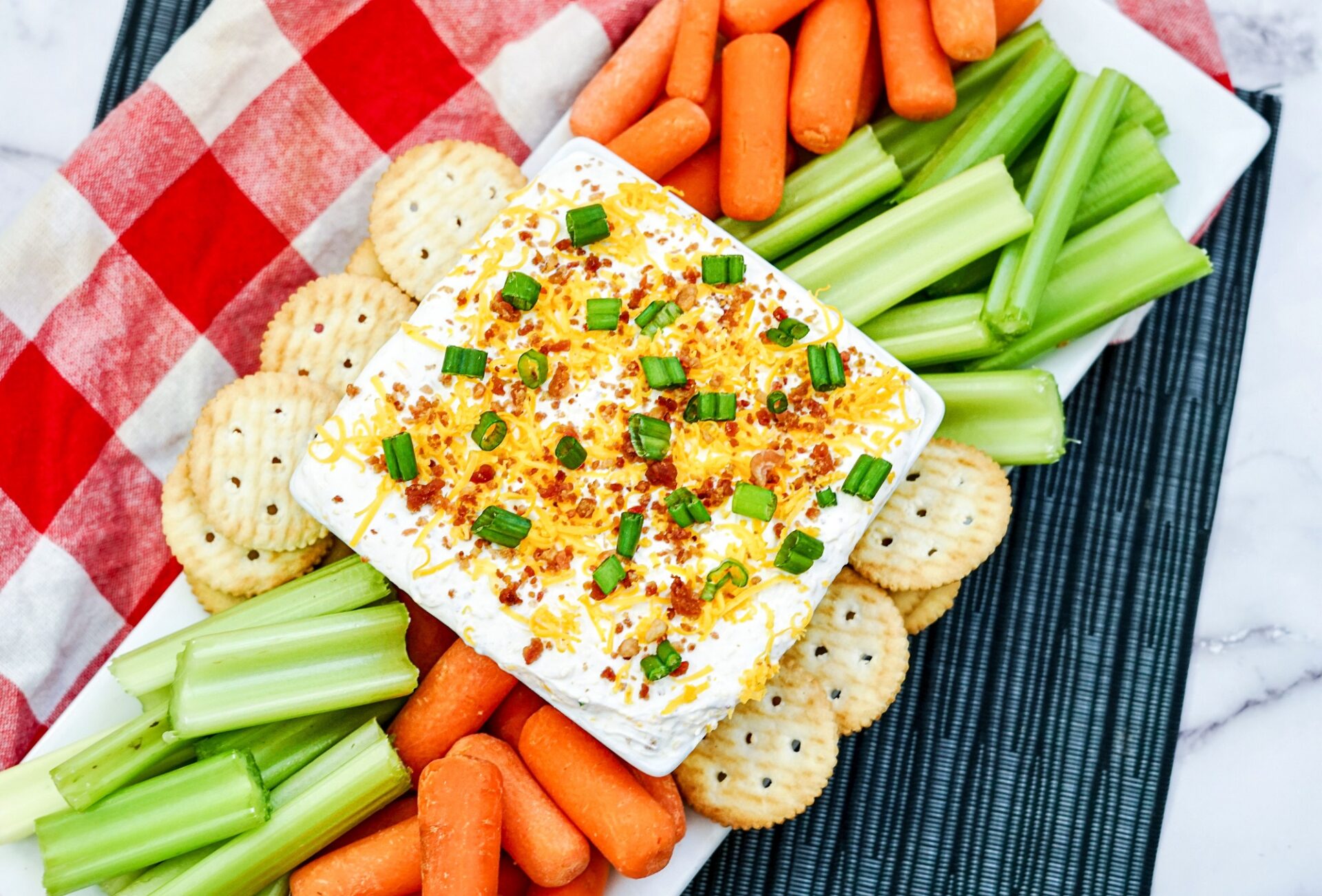 Cheddar Bacon Ranch Dip in a bowl surrounded with crackers, carrots and celery.