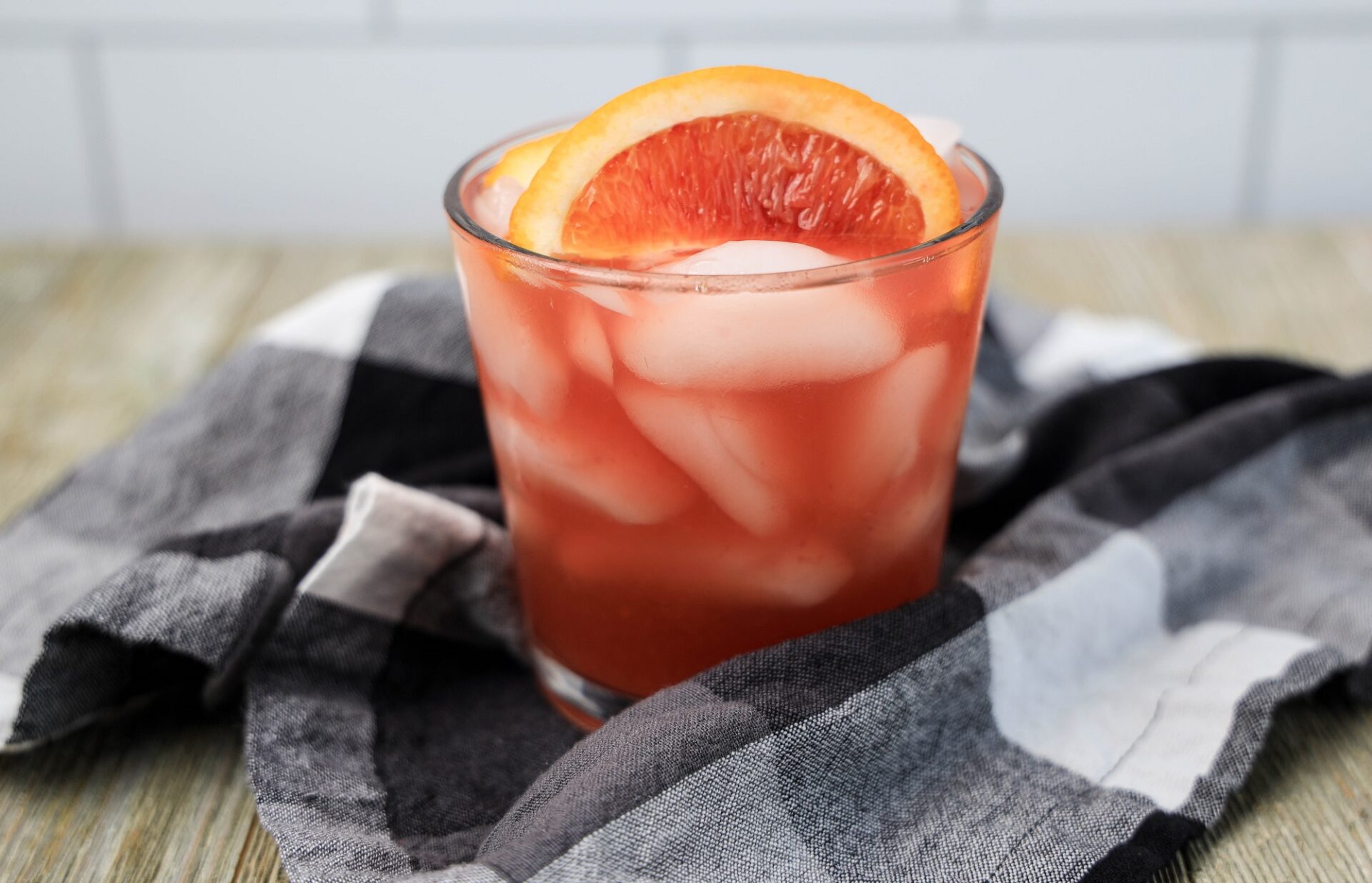 Blood orange bourbon cocktail on a counter with a black and white checkered towel.