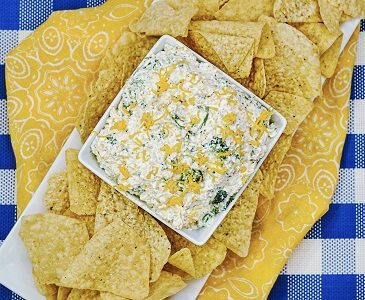 Broccoli cheese dip in a bowl beside tortilla chips
