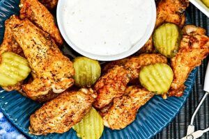 Nashville hot wings with pickle slices and dip on a blue plate.