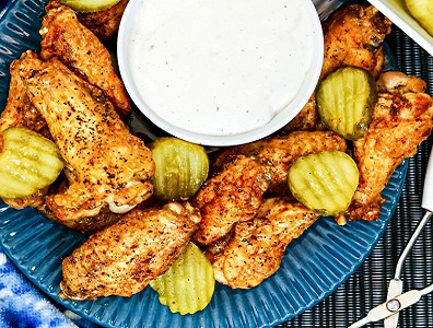 Nashville hot wings with pickle slices and dip on a blue plate.