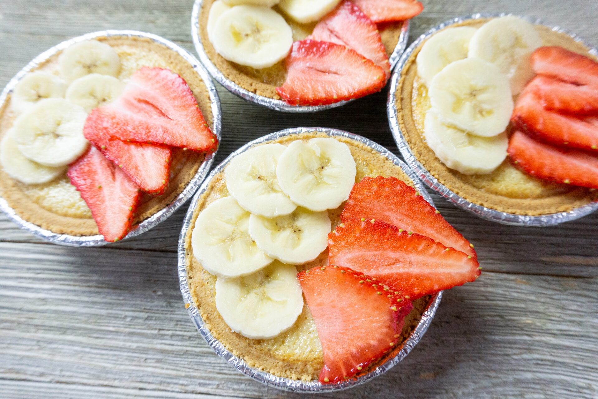 Mini Fruit Tarts with banana and strawberry slices on a wood table