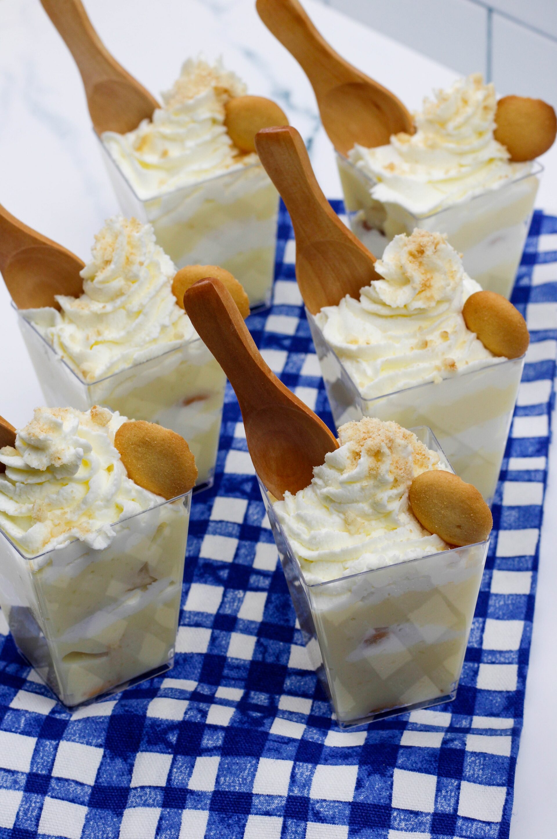 Banana pudding cups on a blue checkered tablecloth.