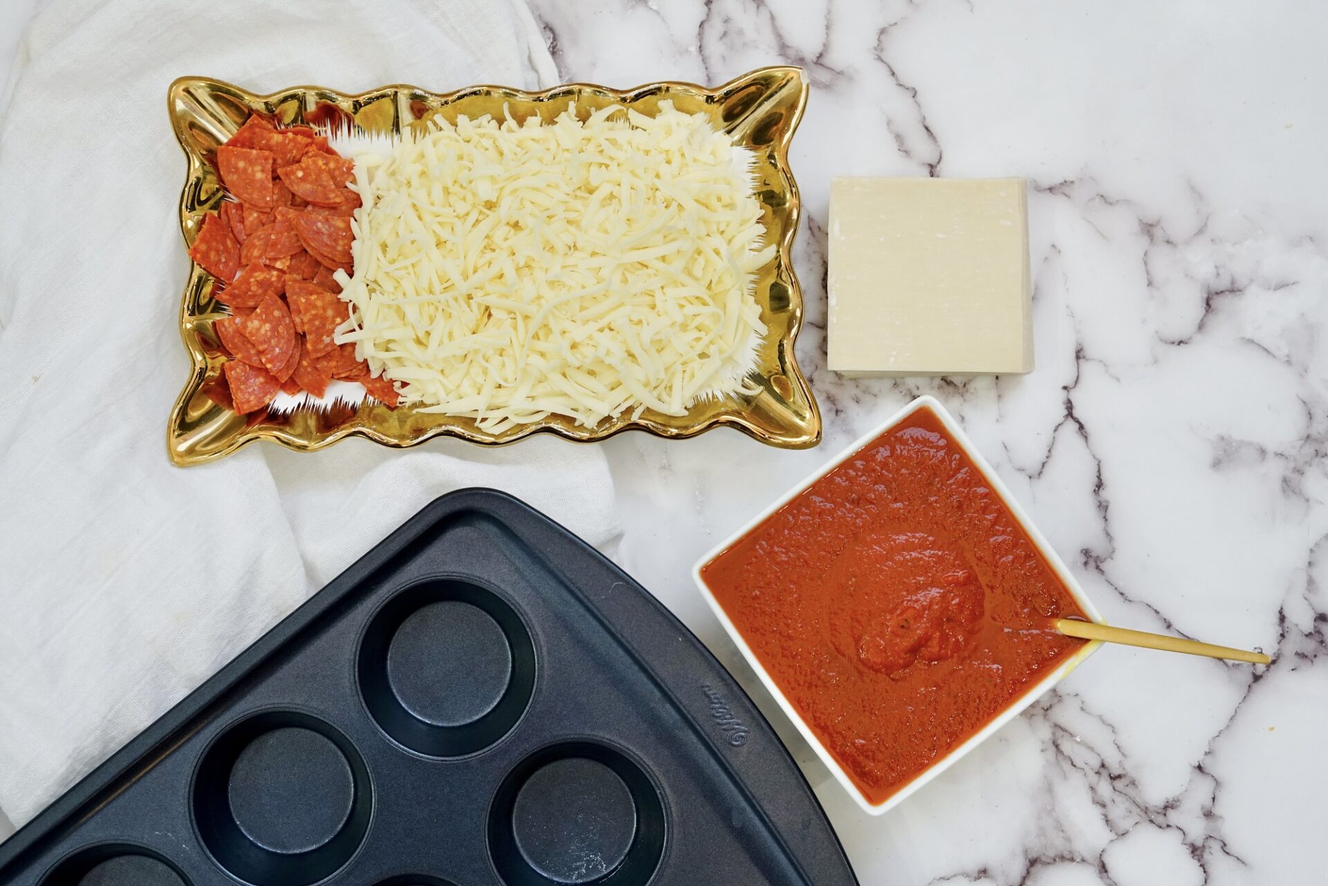 ingredients for wonton pizzas on a counter with a muffin tin.