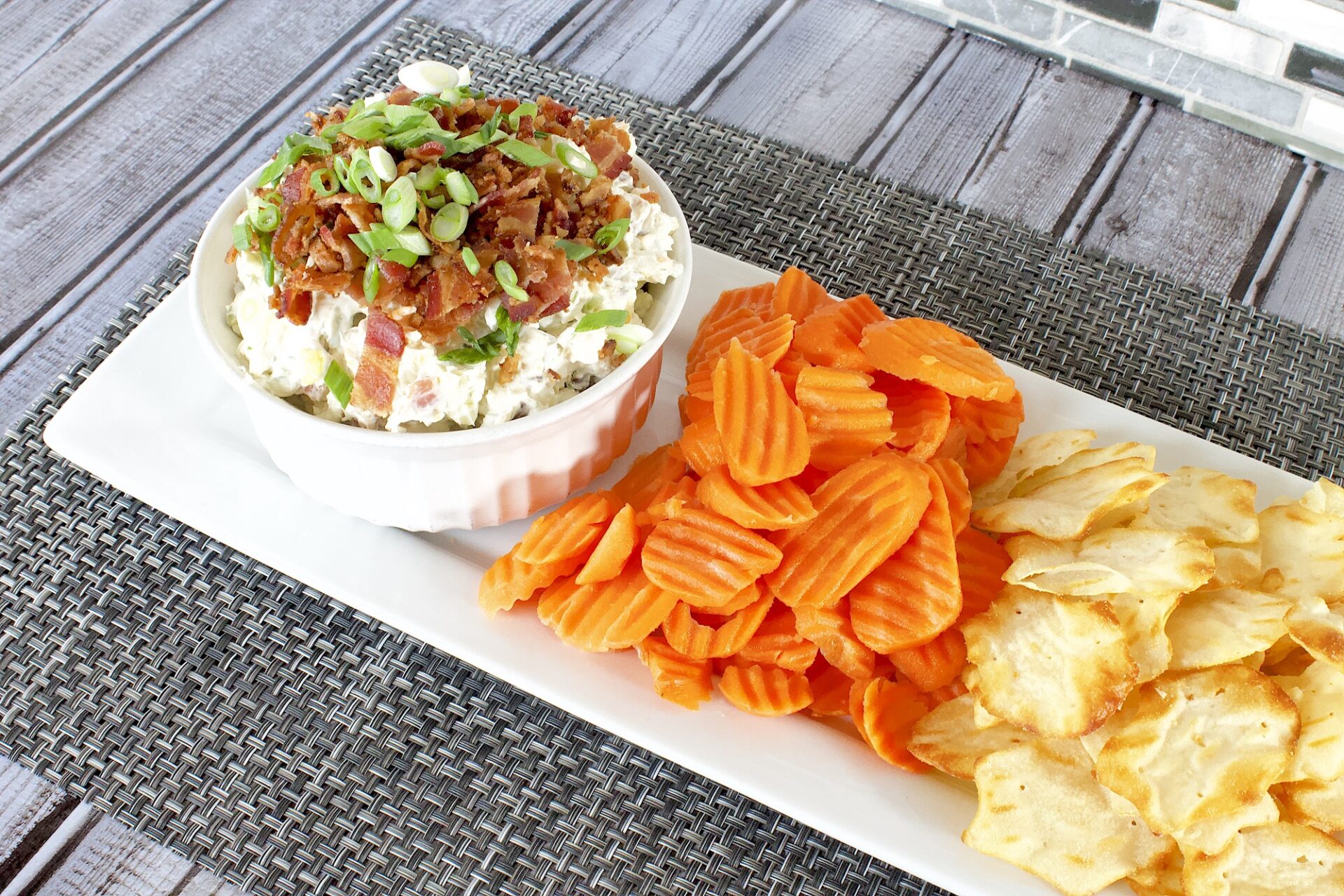 dill pickle dip in a bowl next to carrots and chips.