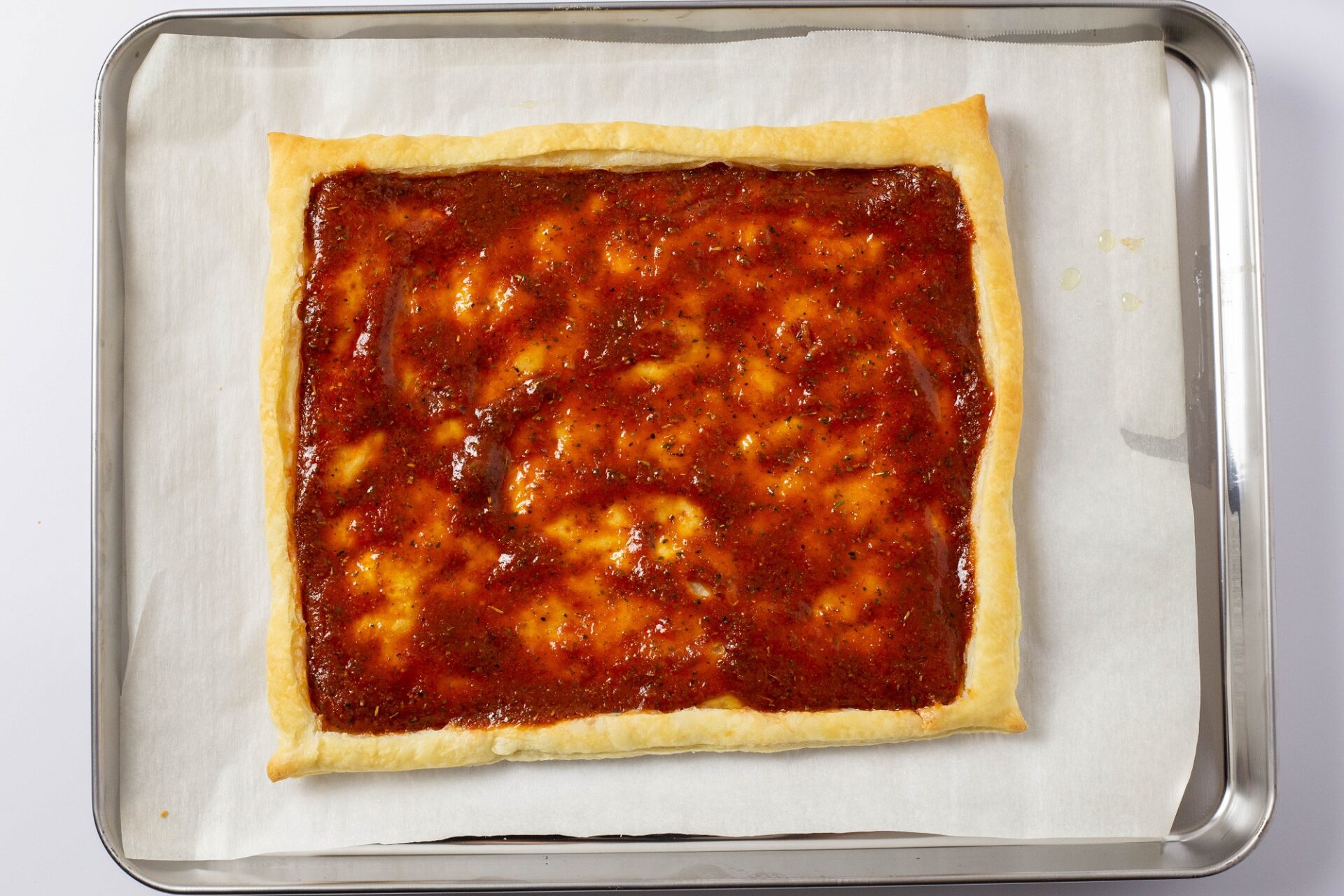 spreading pizza sauce over baked puff pastry crust.