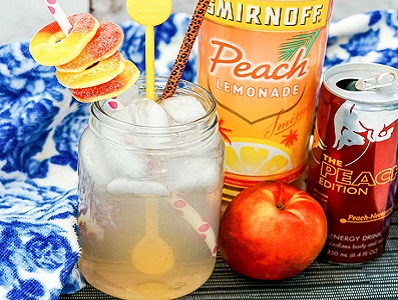 Spiked Peach Red Bull cocktail in a glass with peach candy rings