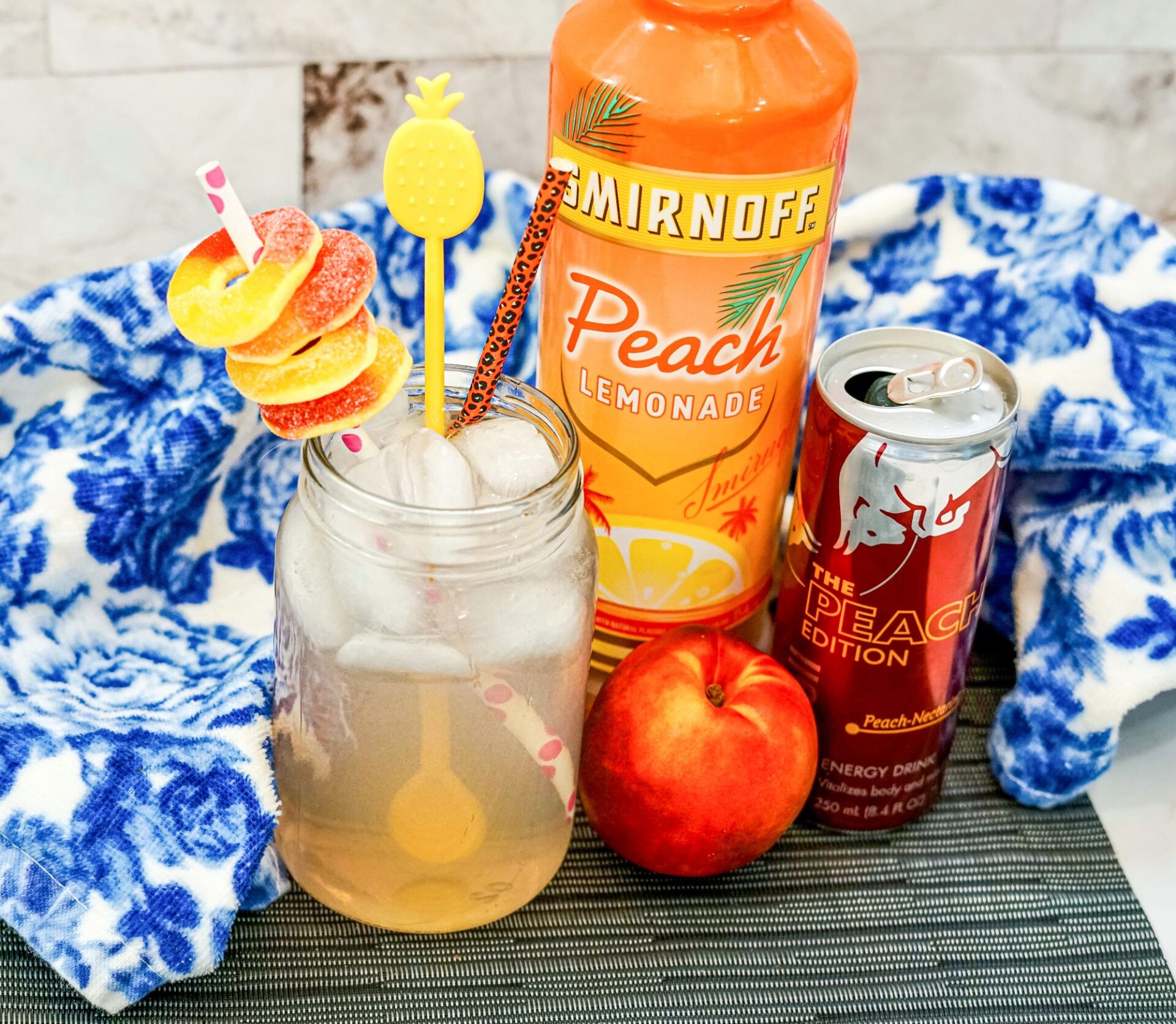 Spiked Peach Red Bull alcoholic drink with peach ring garnish and straws.