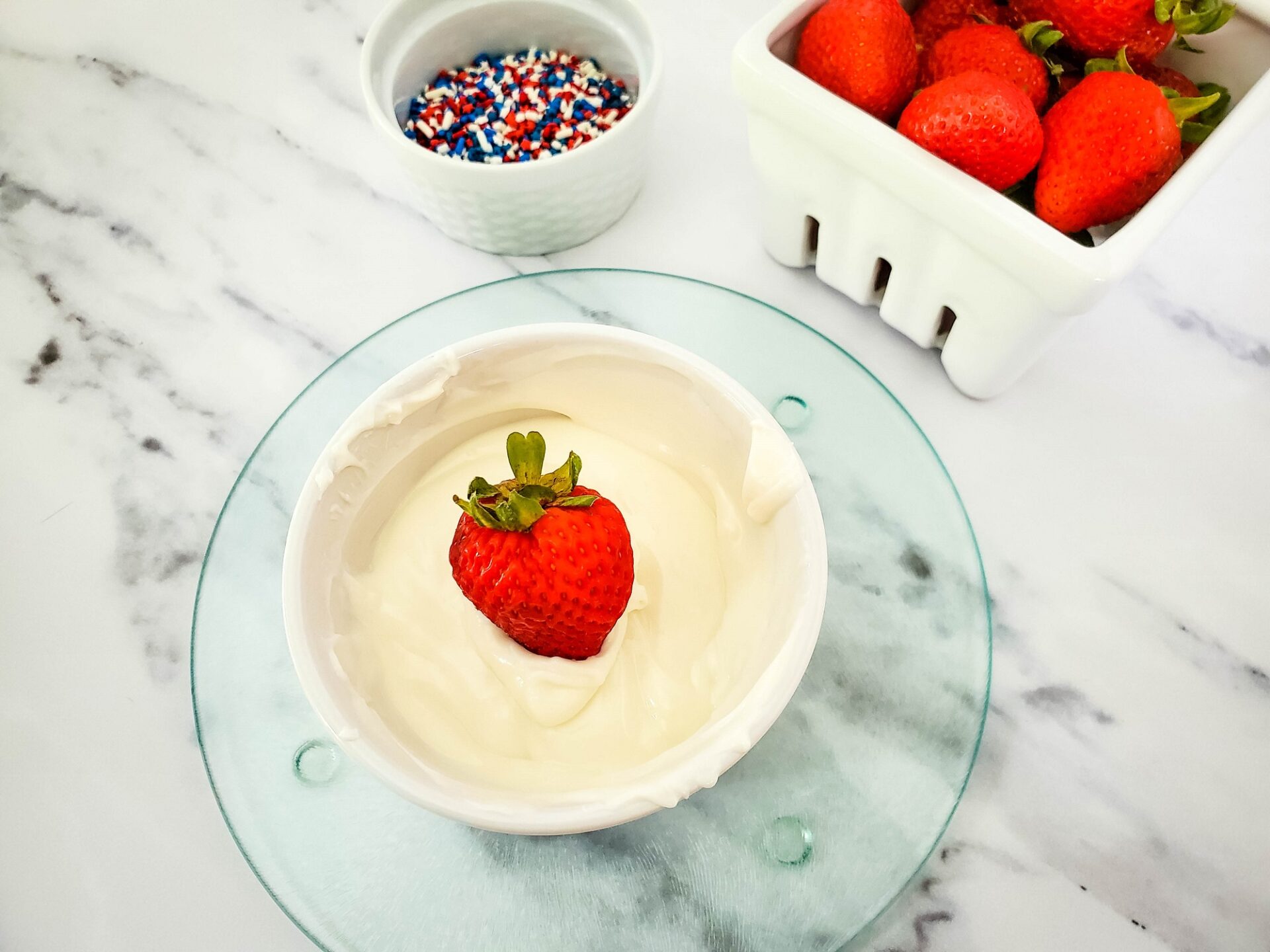 dipping a strawberry into melted white chocolate.