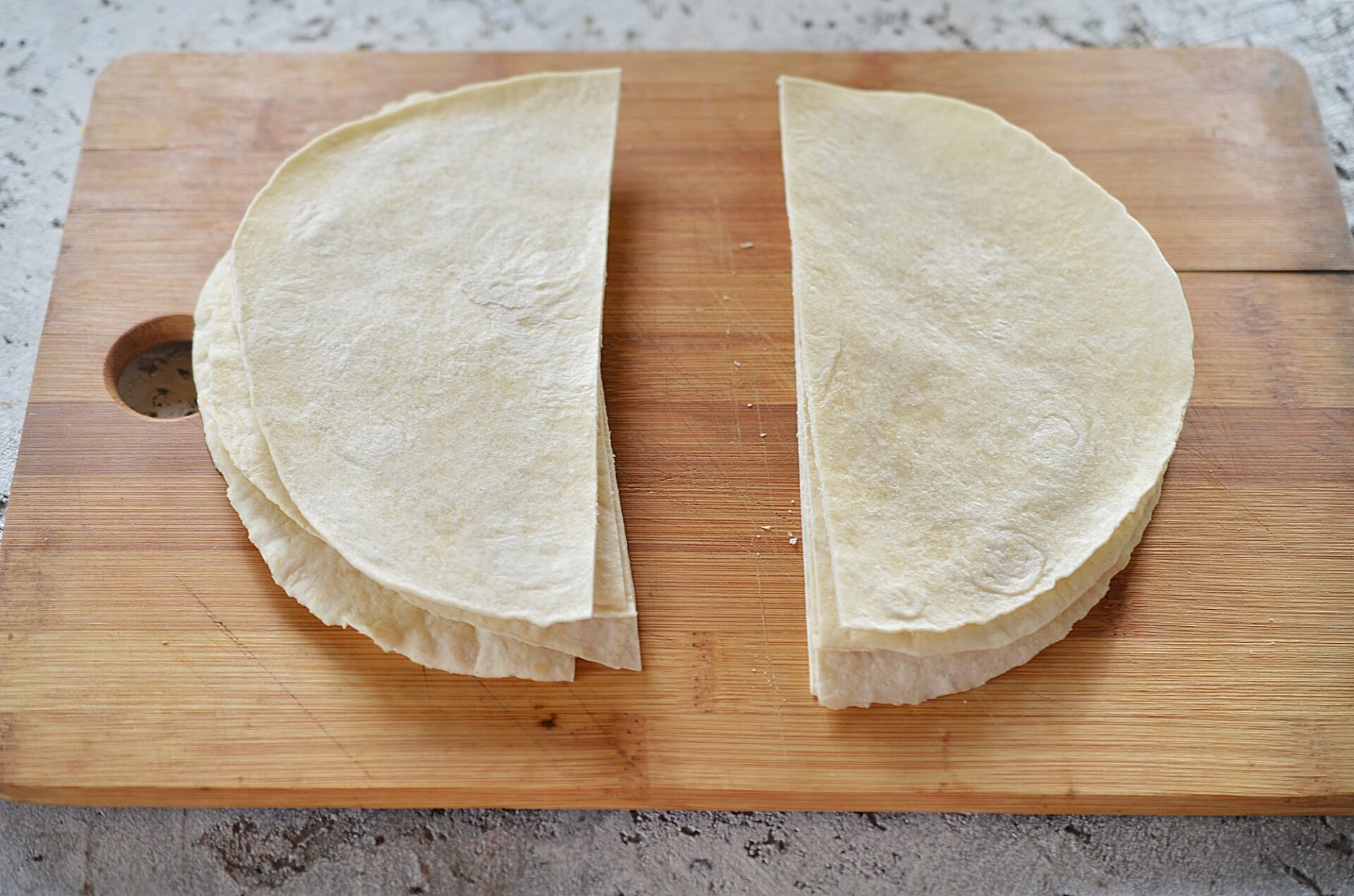 Tortillas cut in half on a cutting board.