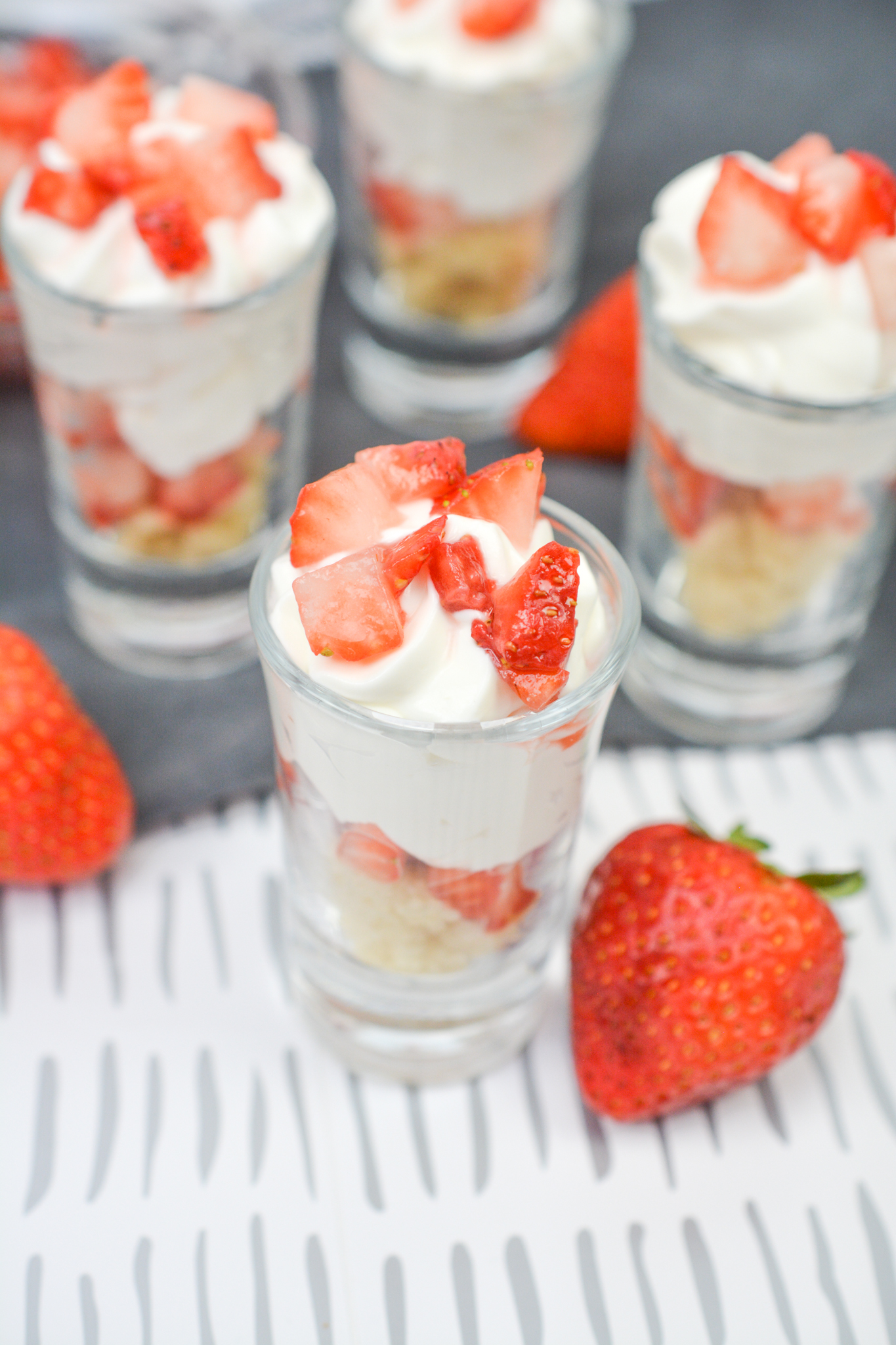 Strawberry shortcake shooters on a counter with strawberries.
