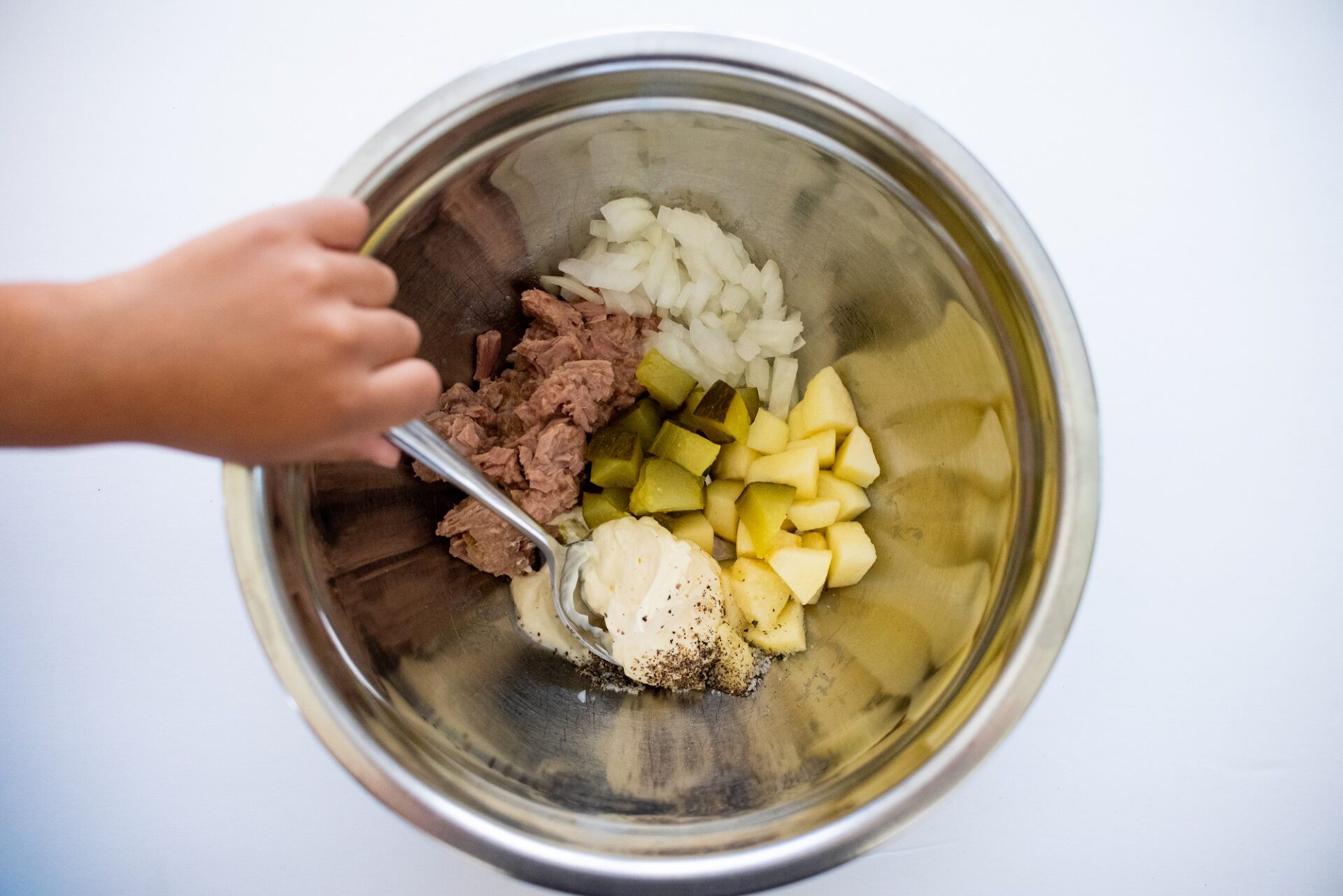 Mixing tuna, onion, apple, pickle and mayo in a metal bowl.