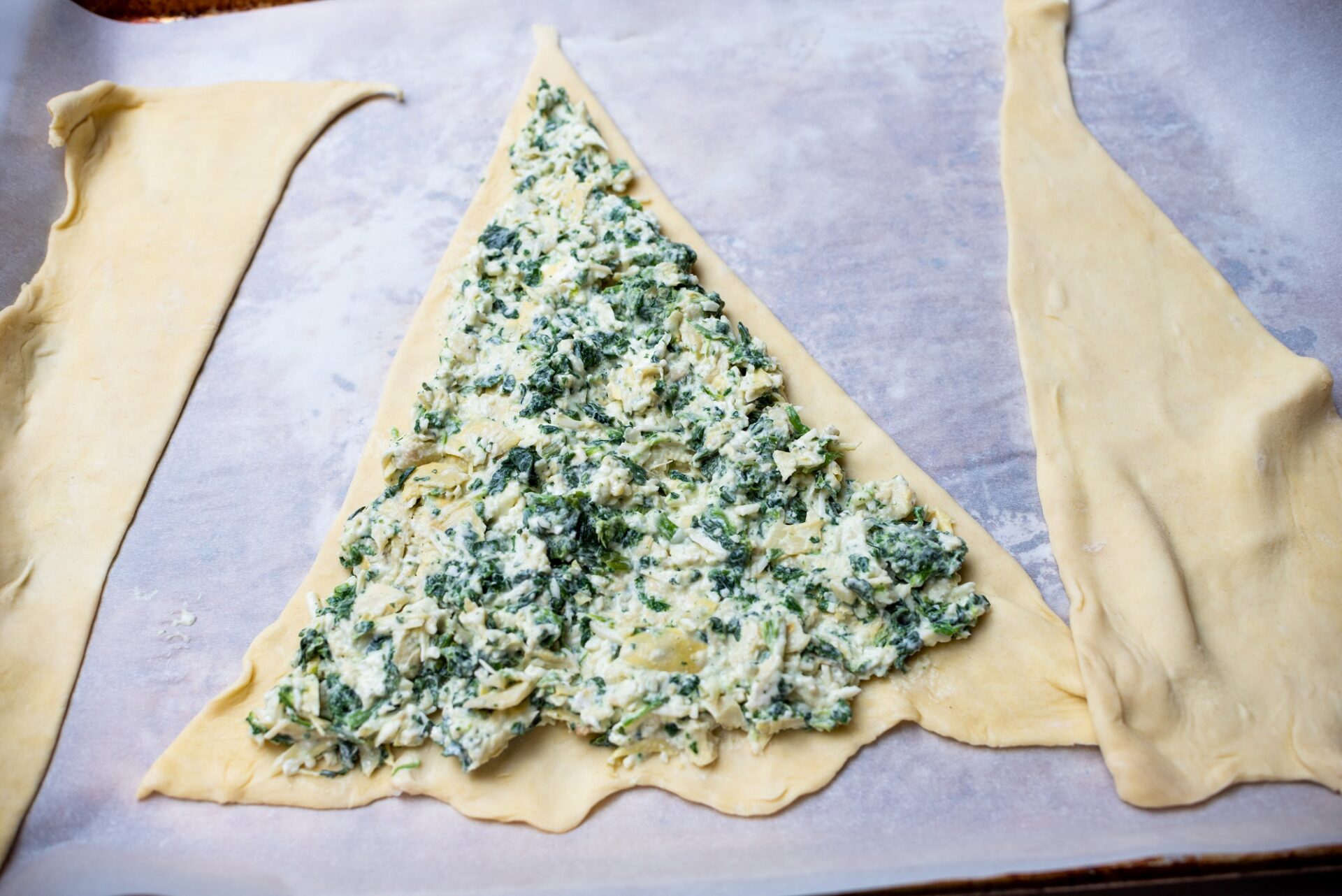 Adding spinach dip to a triangle of puff pastry.