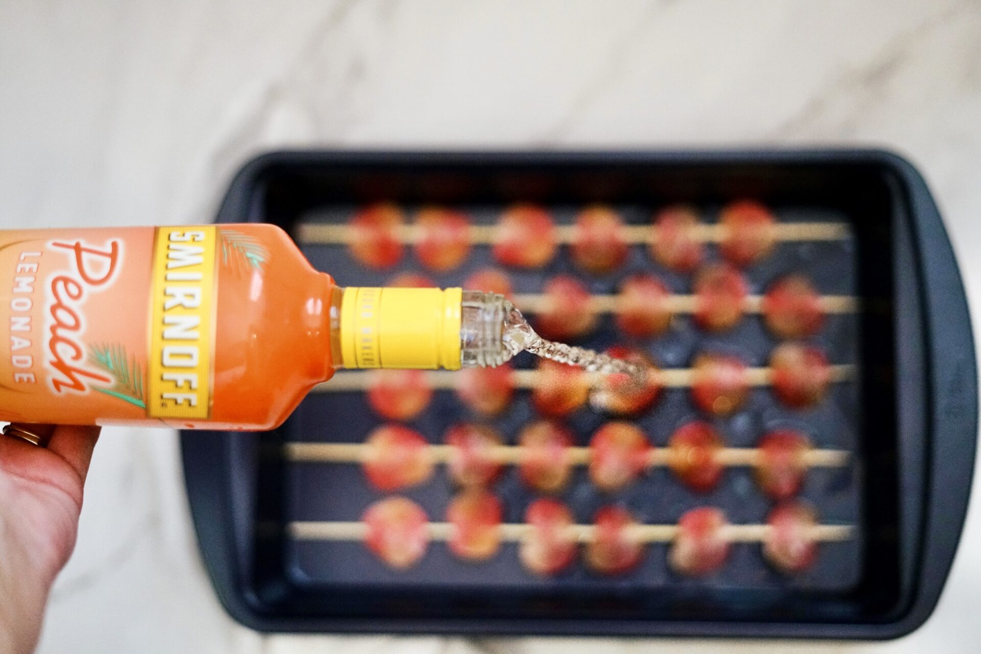 Pouring vodka over skewers of peach gummies.