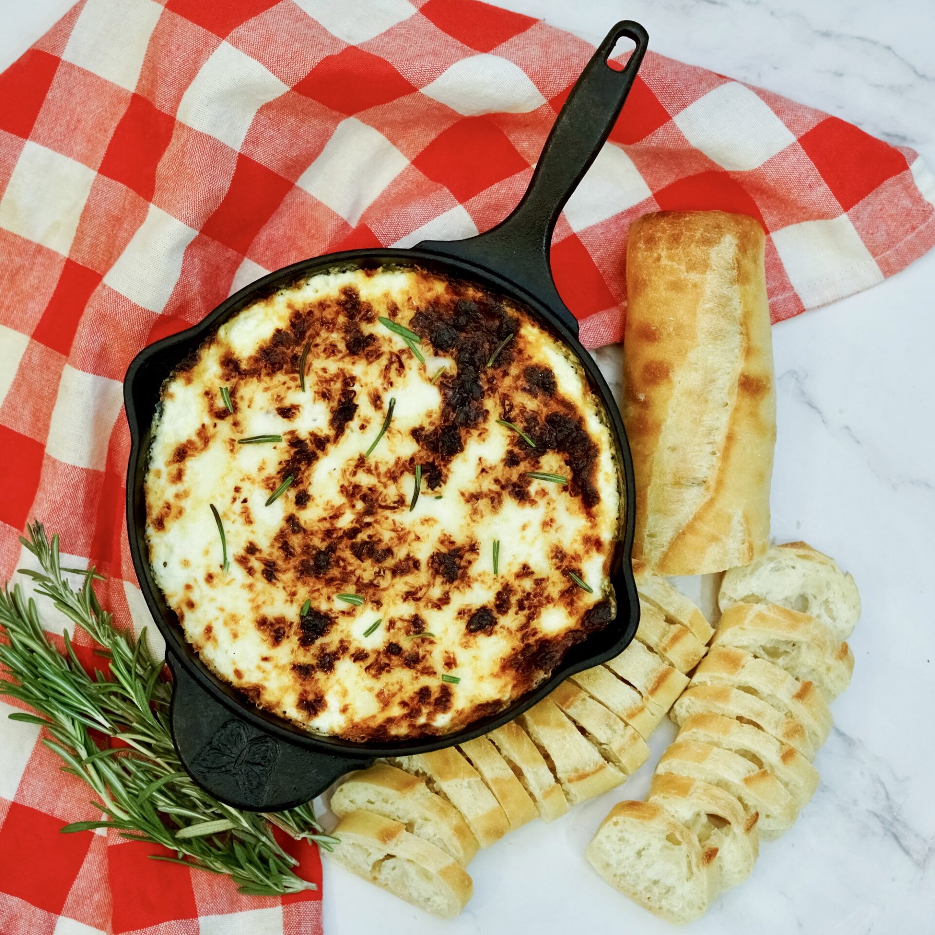 Baked ricotta dip on a counter with bread and rosemary.