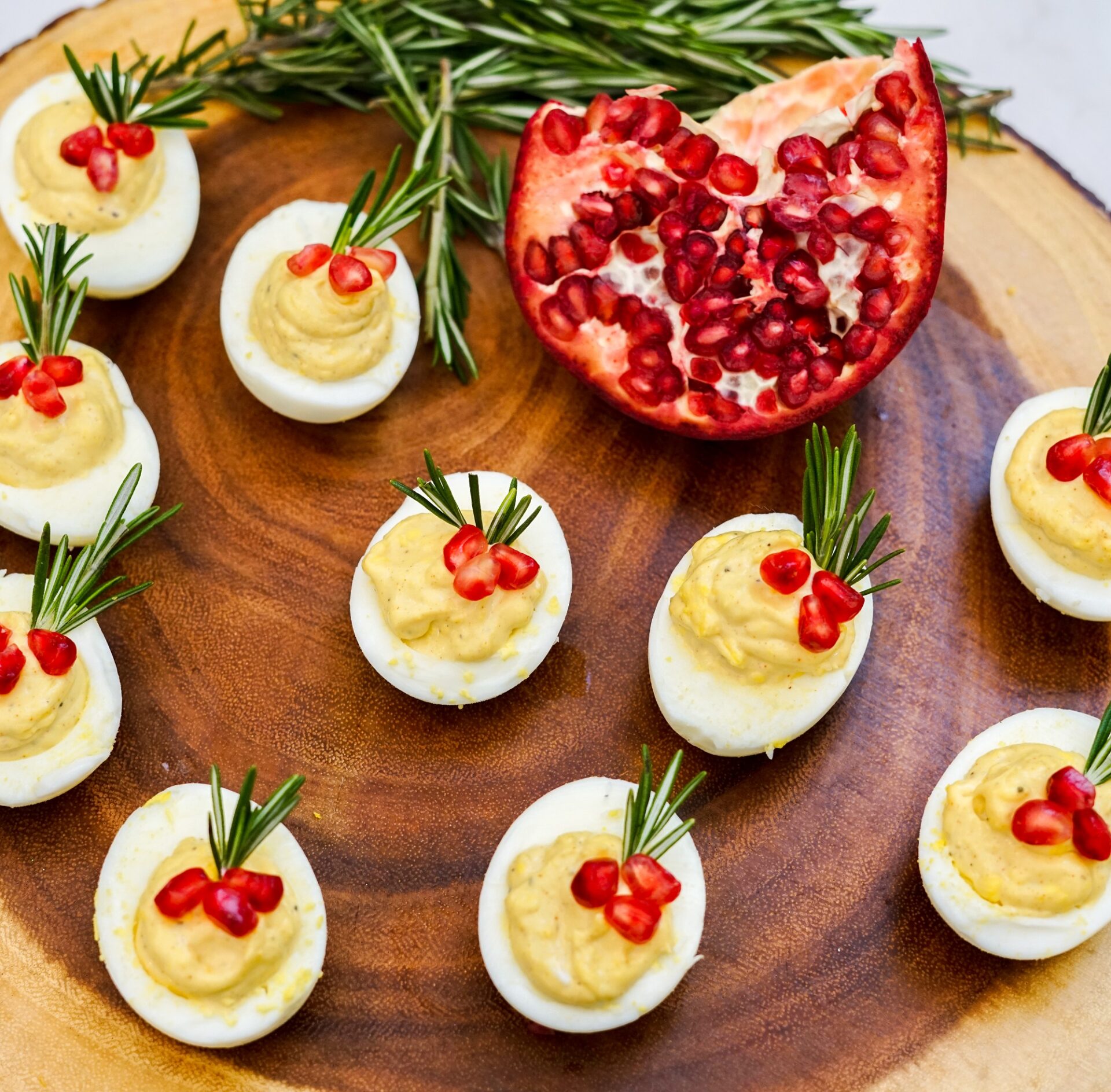 Deviled eggs with rosemary and pomegranate seeds on a wooden board.