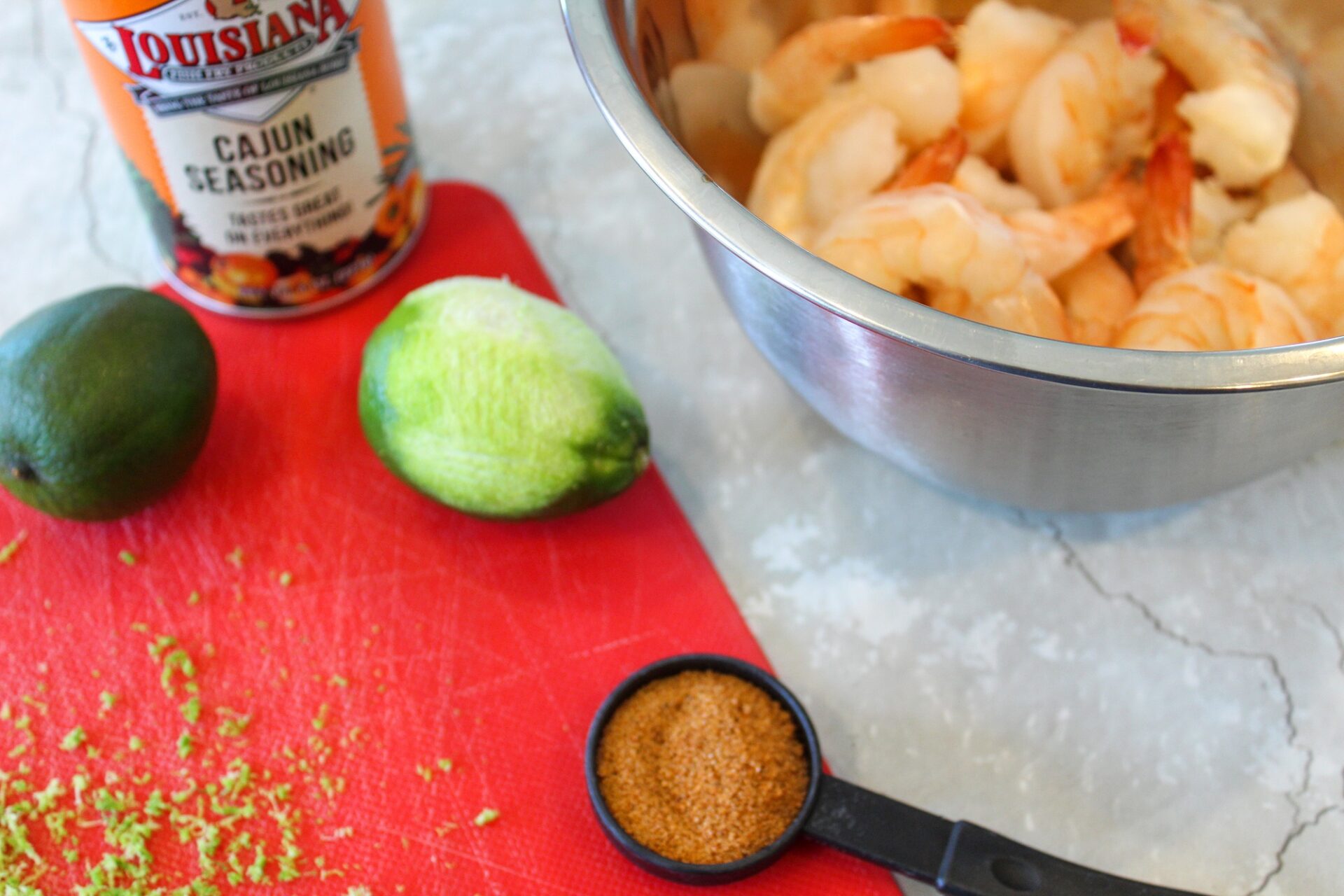 Lime zest and Cajun seasoning on a cutting board next to a bowl of shrimp.
