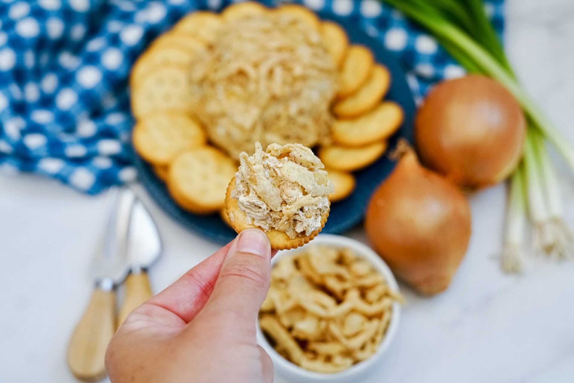 Taking a scoop of french onion cheese ball with a cracker.