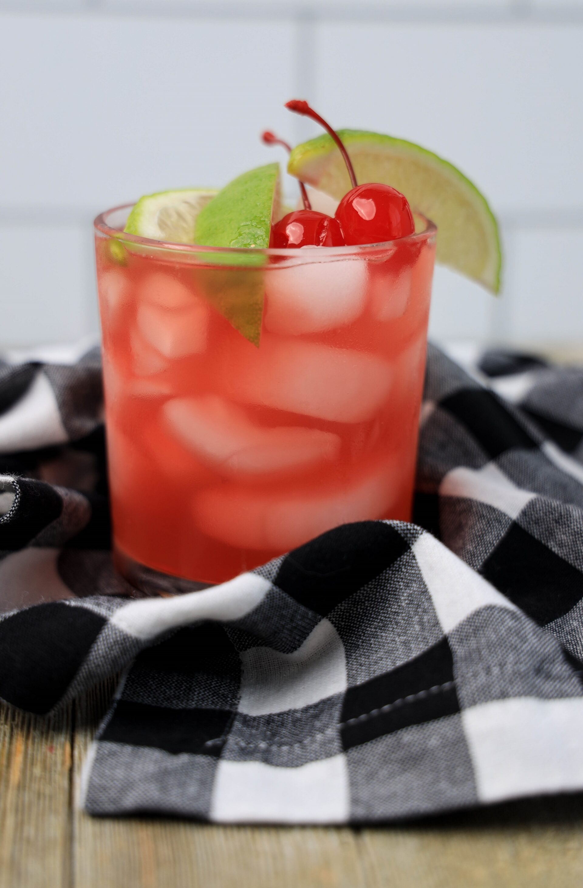 Bourbon cherry limeade cocktail on a counter with a black and white checkered towel.