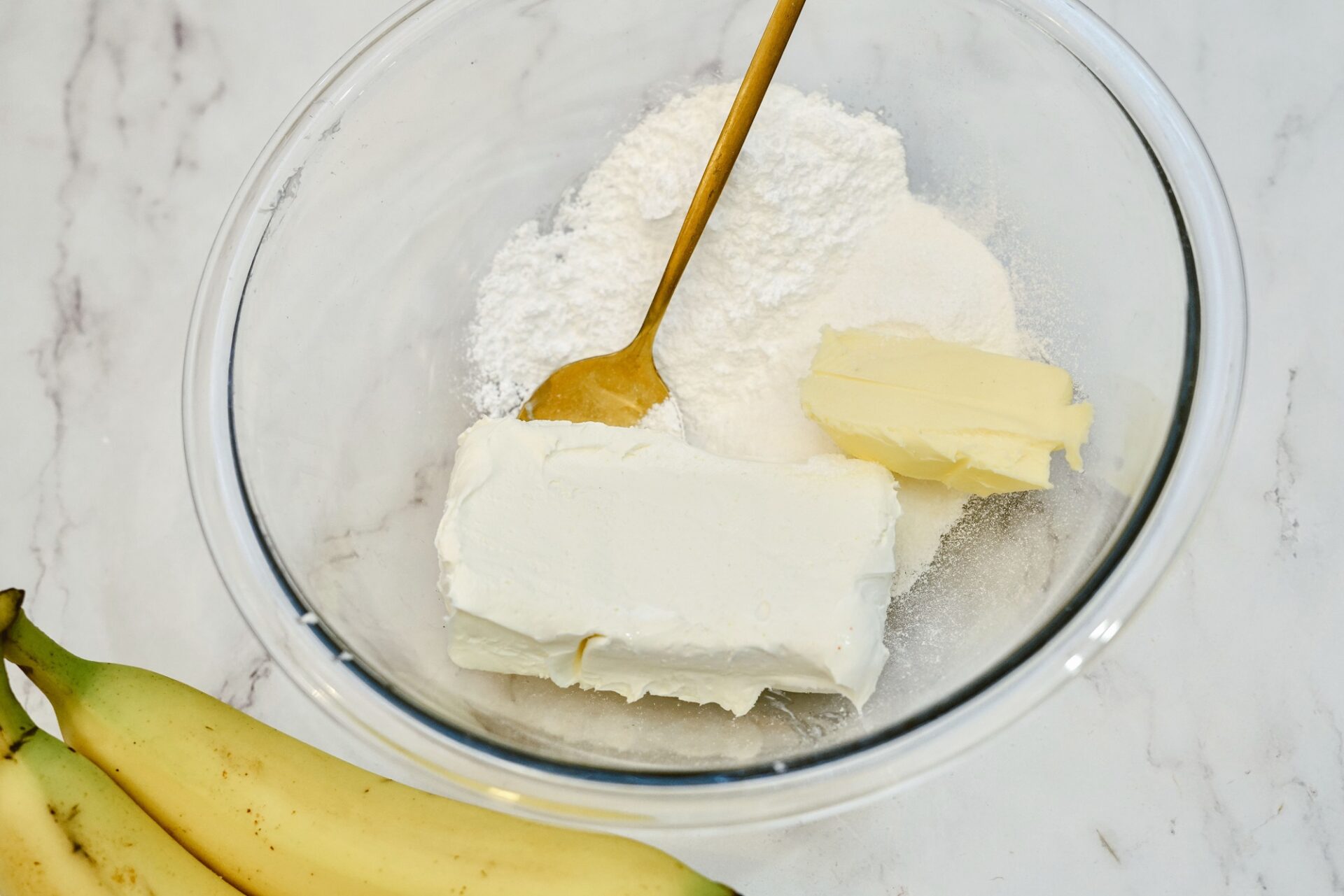 Mixing sugar, cream cheese, butter, and pudding mix in a glass bowl.