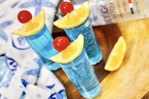 Blue Kamikaze shot in shot glass with cherry and lime garnish