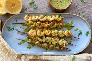 Chimichurri Shrimp Grilled on skewers with Chimichurri Sauce beside it.