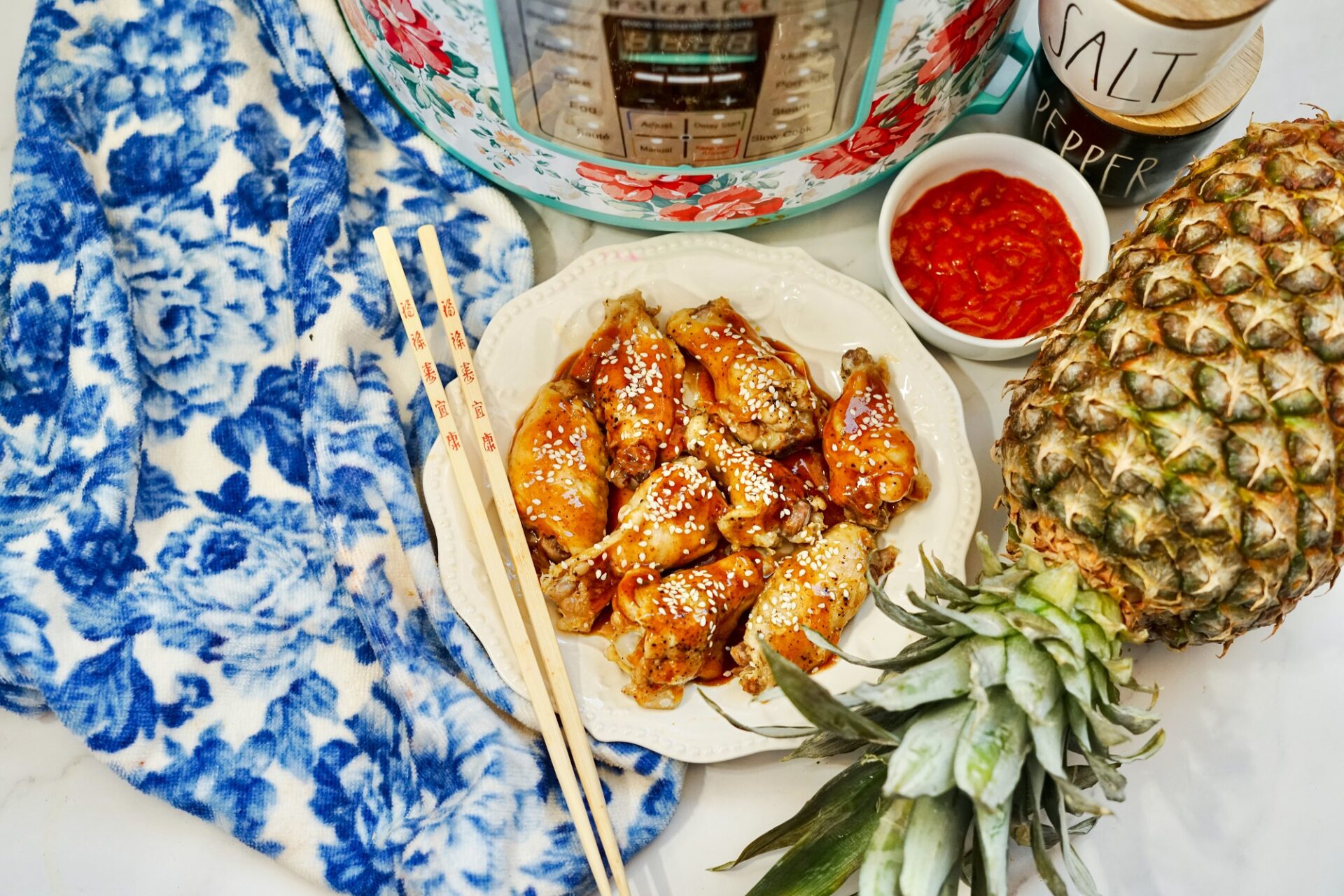 Teriyaki Chicken Wings on a plate in front of air fryer, with dipping sauce beside.