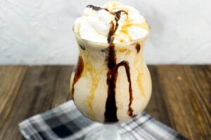 Peanut Butter Whiskey Milkshake in a glass with whipped topping and drizzled chocolate and caramel.