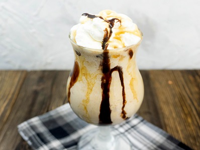 Peanut Butter Whiskey Milkshake in a glass with whipped topping and drizzled chocolate and caramel.