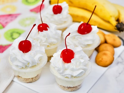 Banana Pudding shots with 99 Bananas, whipped cream and cherry garnish on a plate