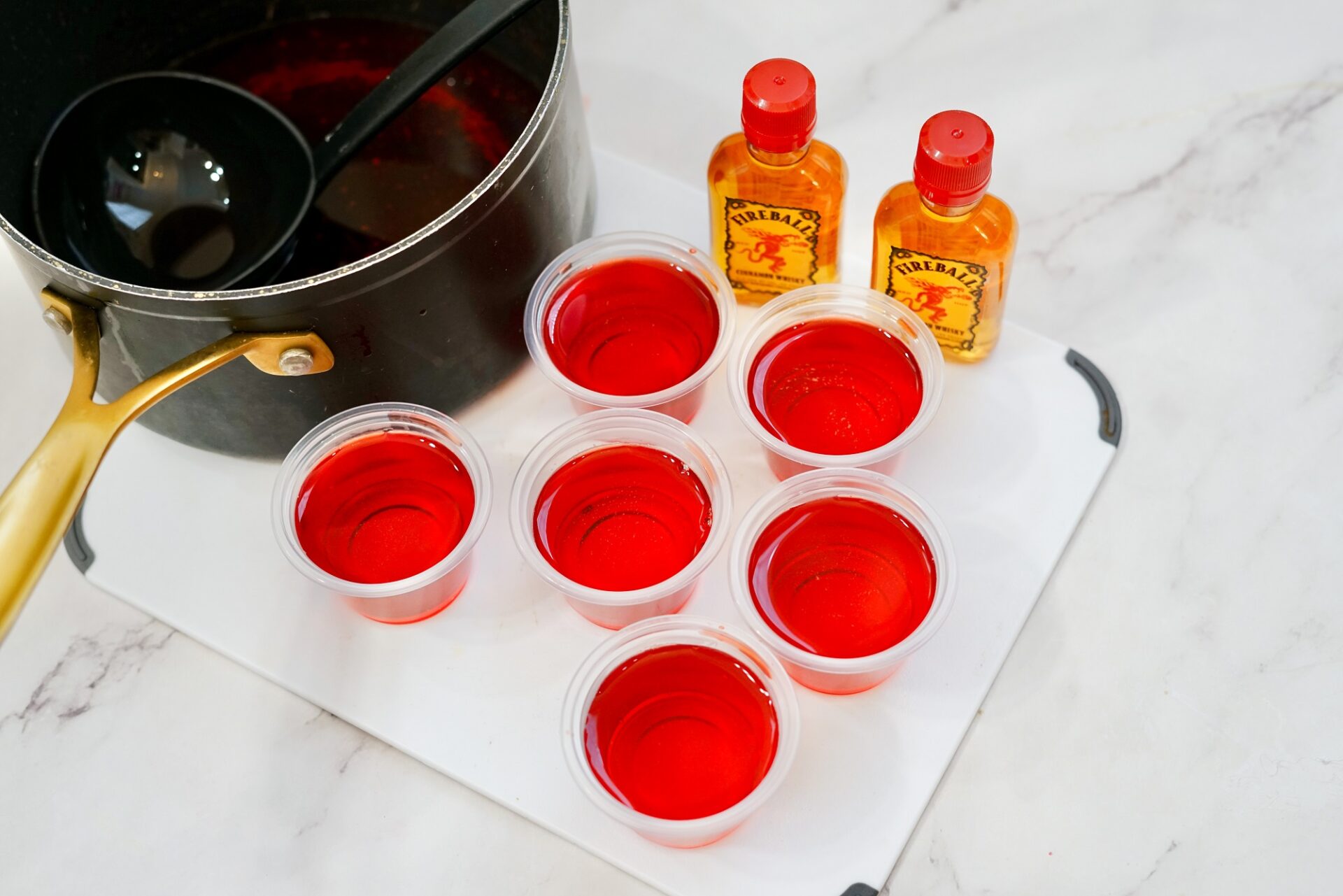 Using a ladle to transfer jello mixture to plastic shot cups.