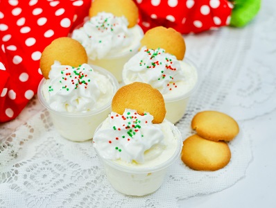 Cinnamon Vodka Pudding shots with cookie garnish, whipped cream and sprinkles on a lace covered tray.