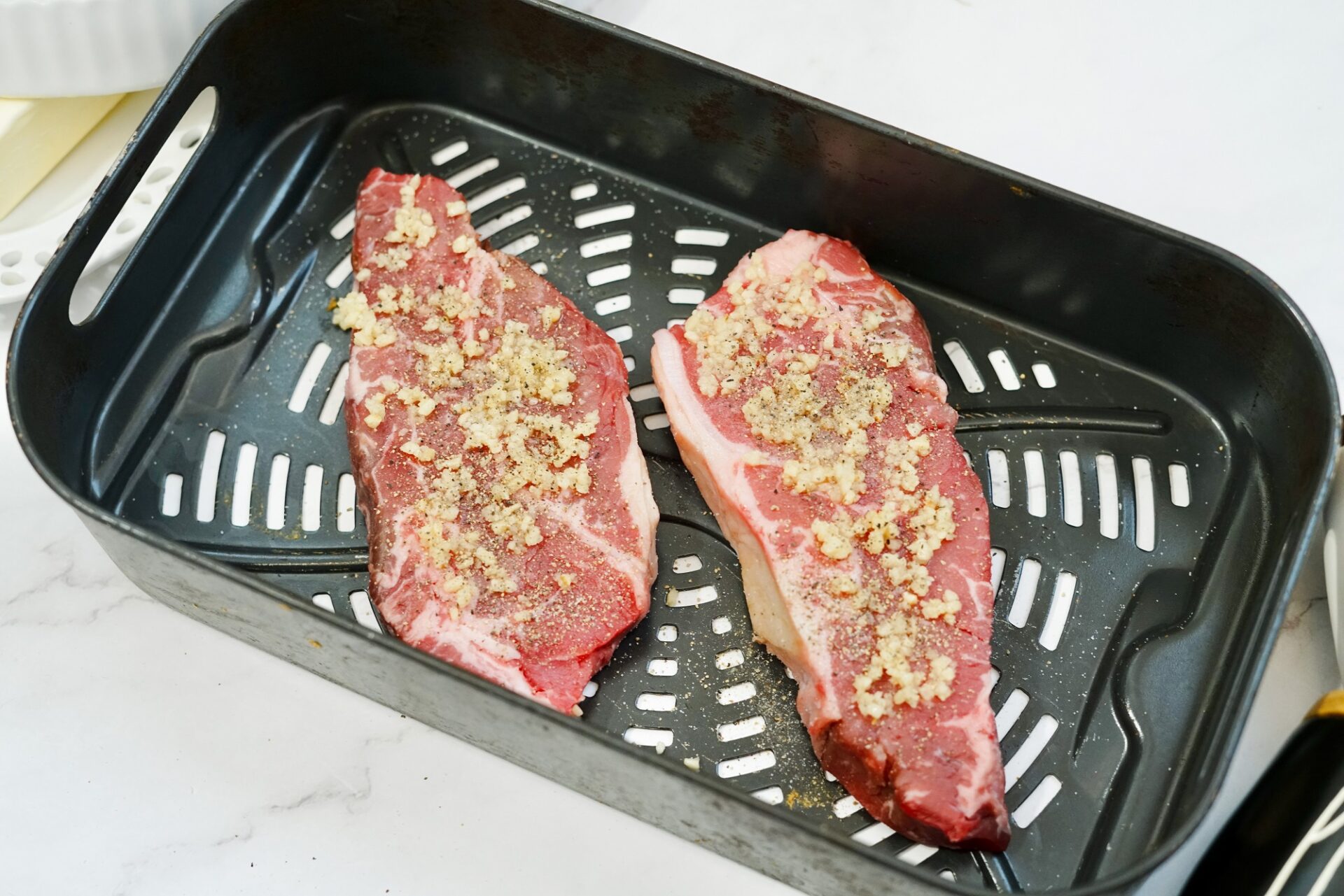 Two uncooked prepared steaks in the air fryer basket.