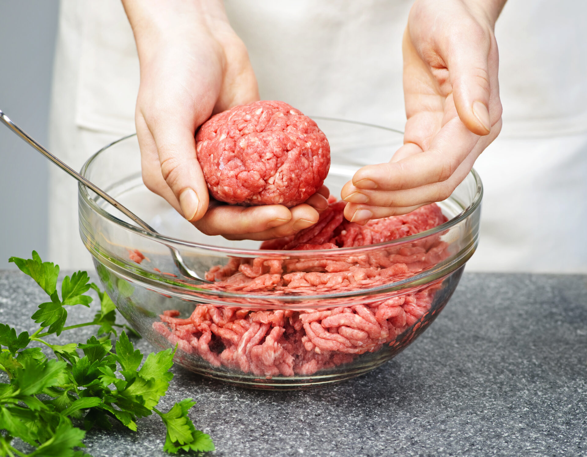 Using hands to form a patty from ground beef in a glass bowl.
