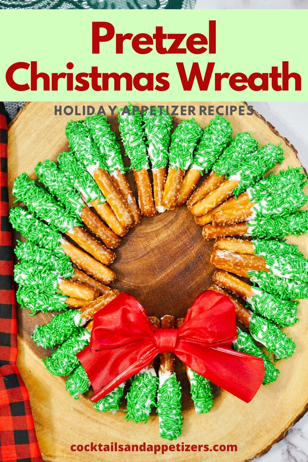 Pretzel wreath with white frosting and green sprinkles and a red bow on a table.