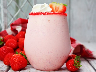 Baileys Strawberries and Cream milkshake in a glass with a sugared rim. A bit of whipped cream and a strawberry for garnish.