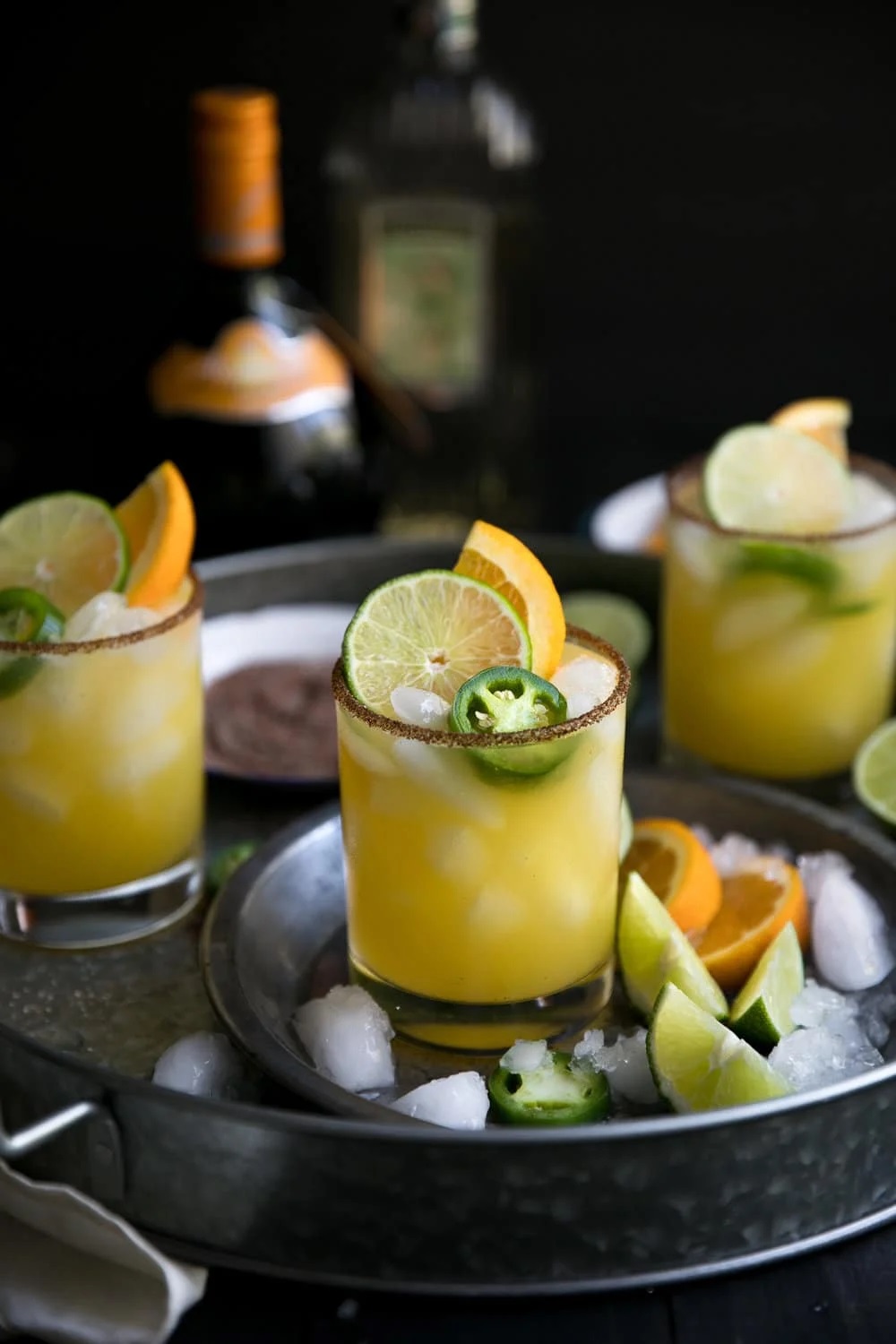 Spicy Orange Margarita in glass with lots of ice, a slice of orange and lime and a slice of pepper for garnish.