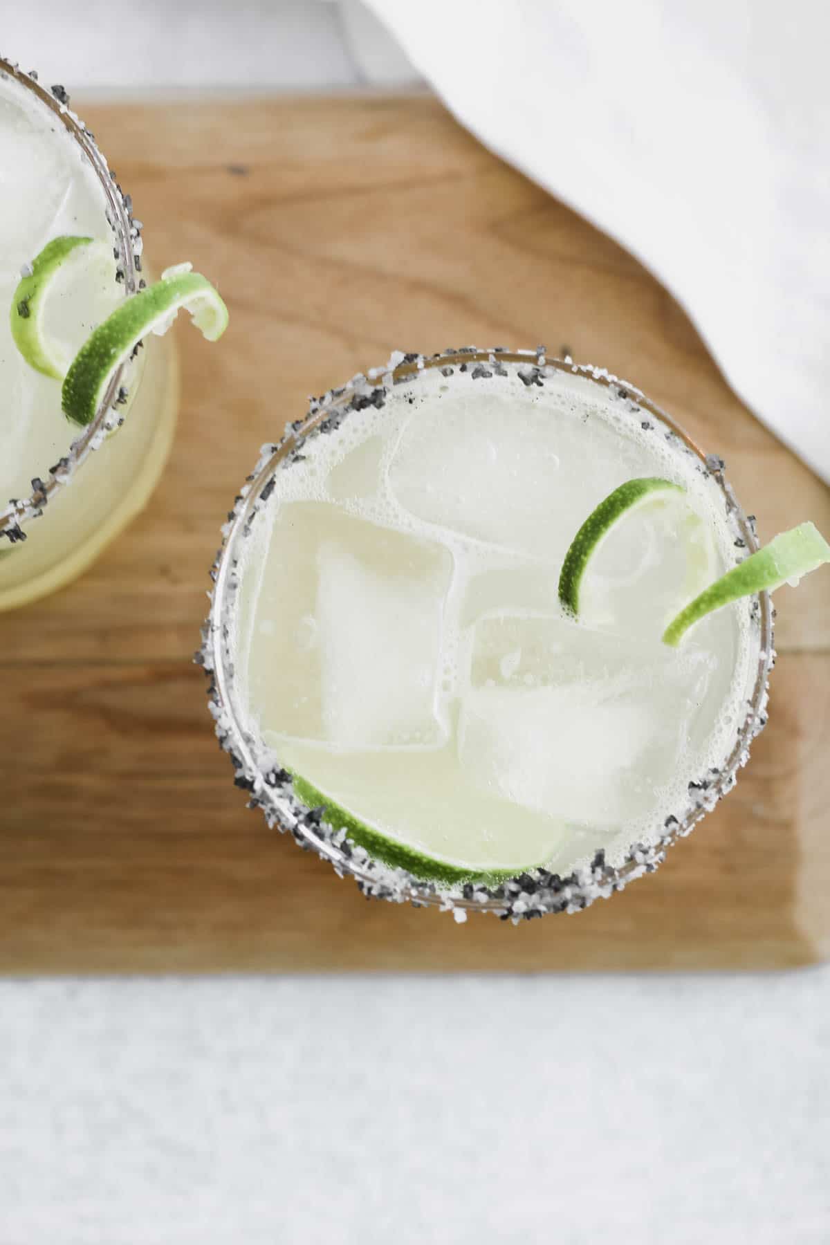 Skinny Topo Chico Margaritas in glasses with salted rim and a curled lime peel slice garnish.