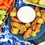 Air Fryer appetizer collection including these spicy chicken wings surrounded by fresh vegetable slices and a dipping sauce.