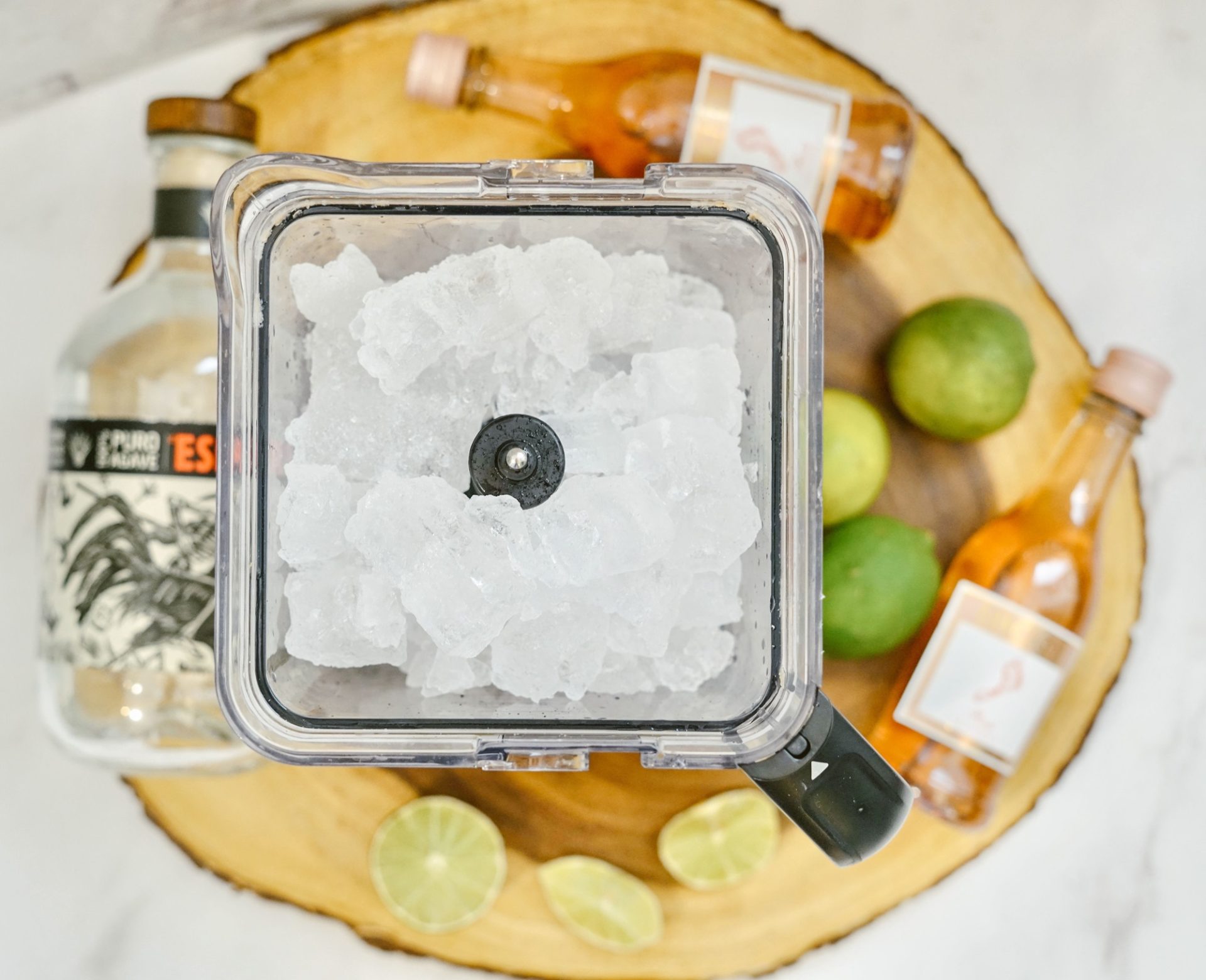 Rosé Margarita ingredients around ice in blender. Tequila, limes, mini bottles of Rose beside.