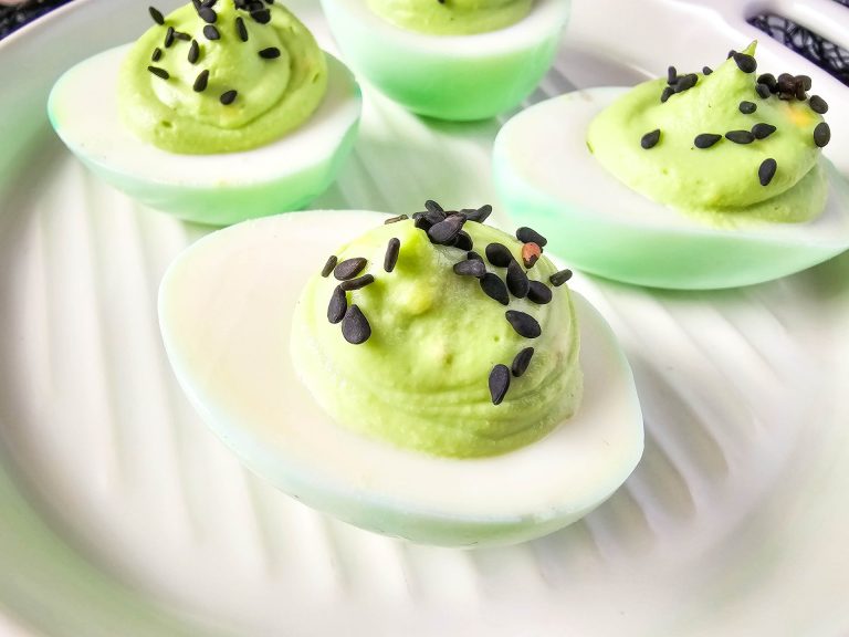 Green Deviled eggs with black sprinkles sit on white plate.