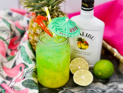 Malibu Blue Hawaiian cocktail with a green drink umbrella sits on a wood table.