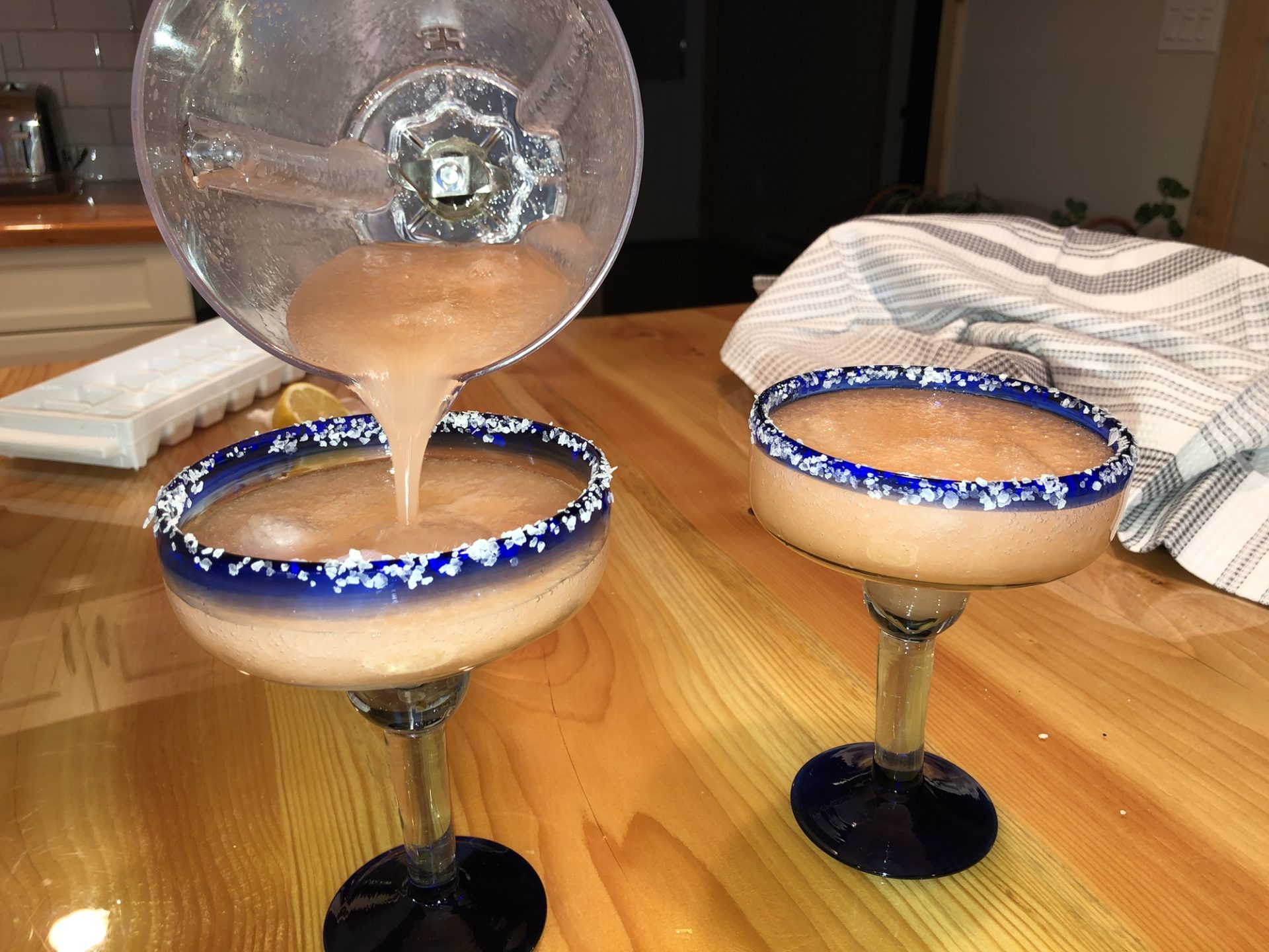 Pouring watermelon margaritas into rimmed glasses.